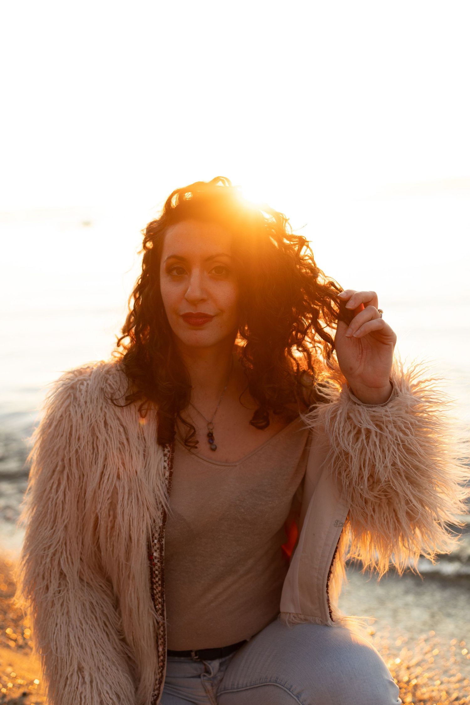 Two people laughing together on a beach at sunset with warm golden light and one wearing a fluffy coat.