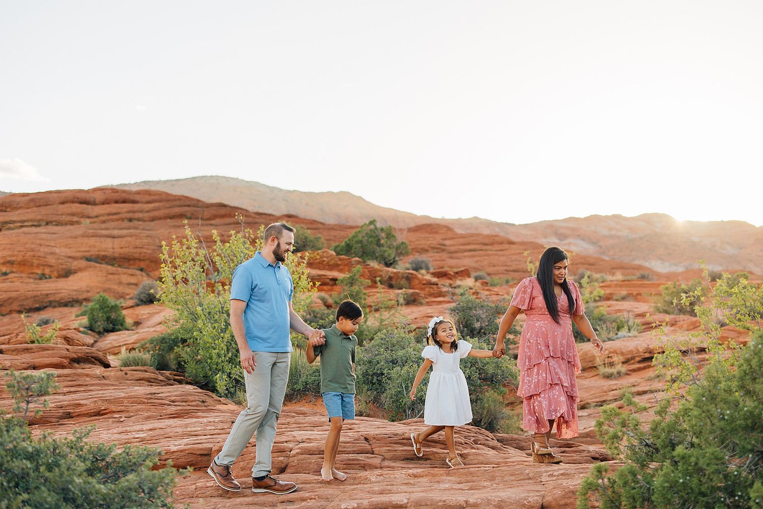 Group walking along scenic desert trail with towering red cliffs in the background.