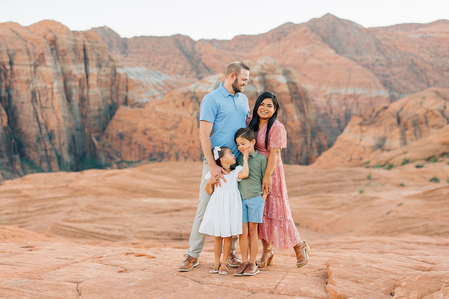 Family exploring red rock formations in a desert landscape during sunset.
