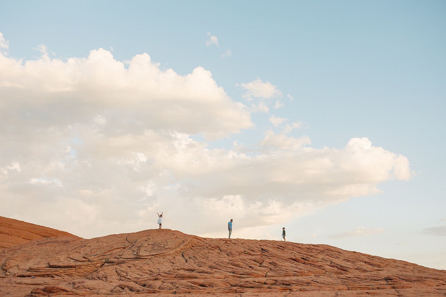Silhouettes of people standing on desert hilltop against blue sky with white clouds.