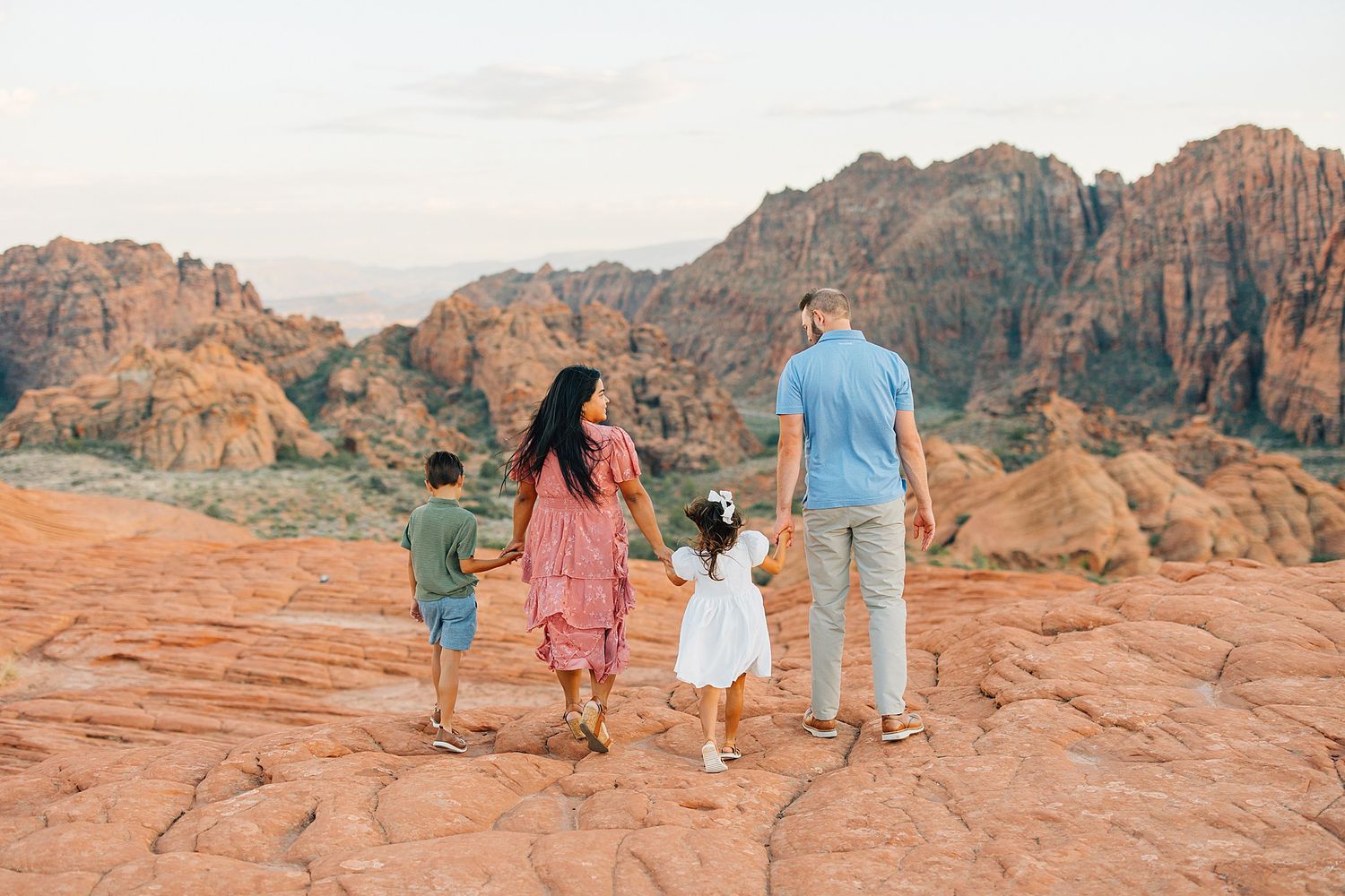 Group walking along desert trail with dramatic red rock cliffs in background.