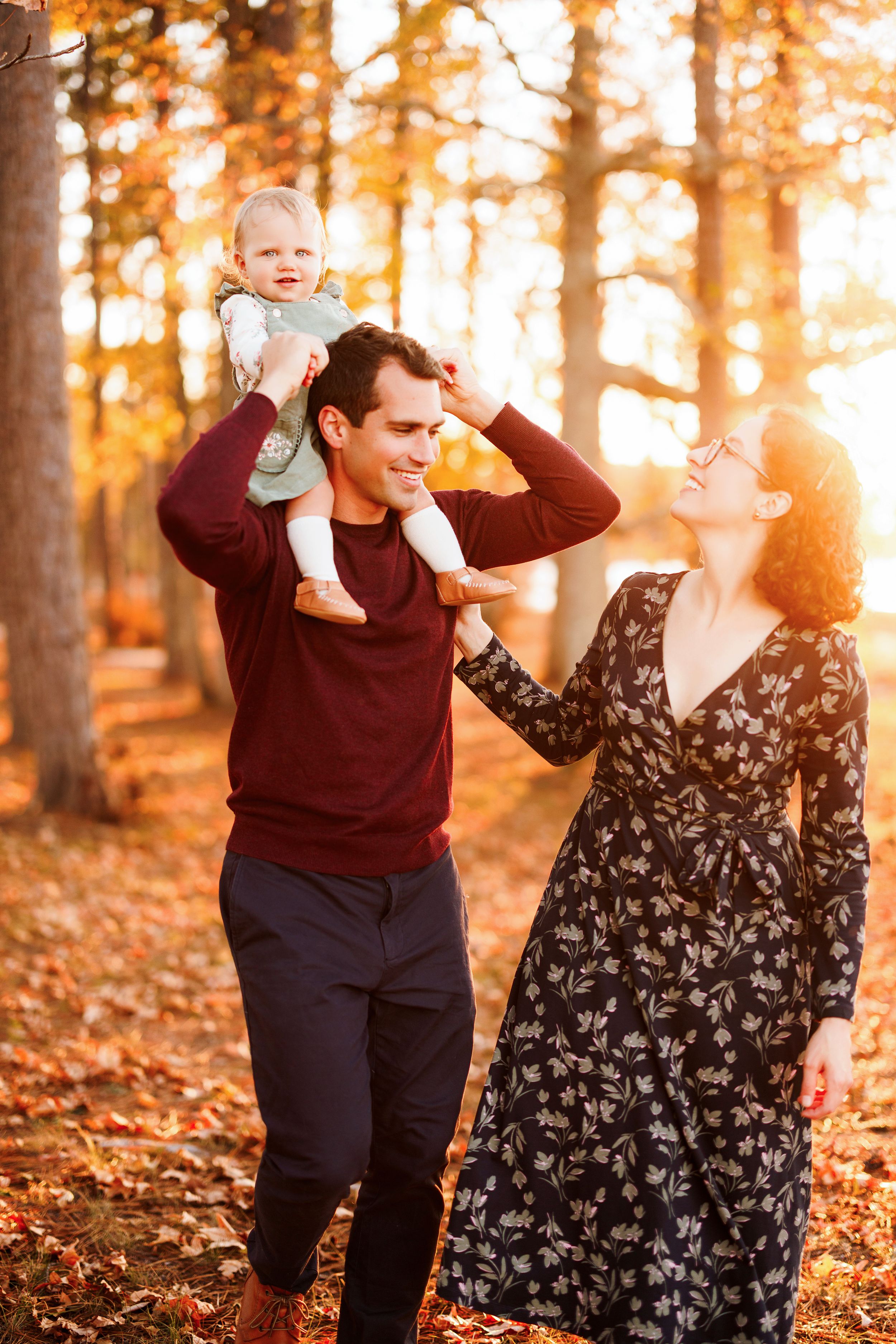 A family enjoys a playful autumn photoshoot in a sunlit forest with golden leaves scattered on the ground.