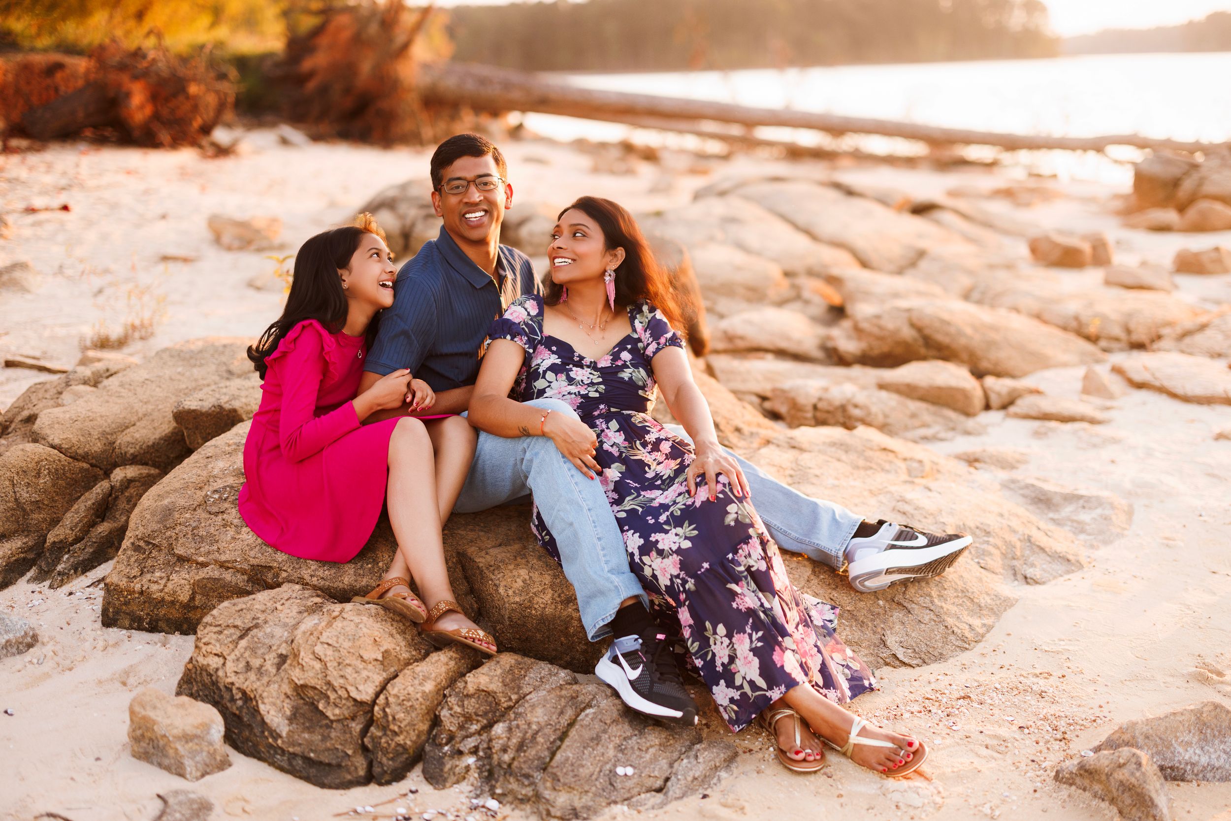 Three people sitting together on coastal rocks at sunset enjoying a relaxed moment by the water.