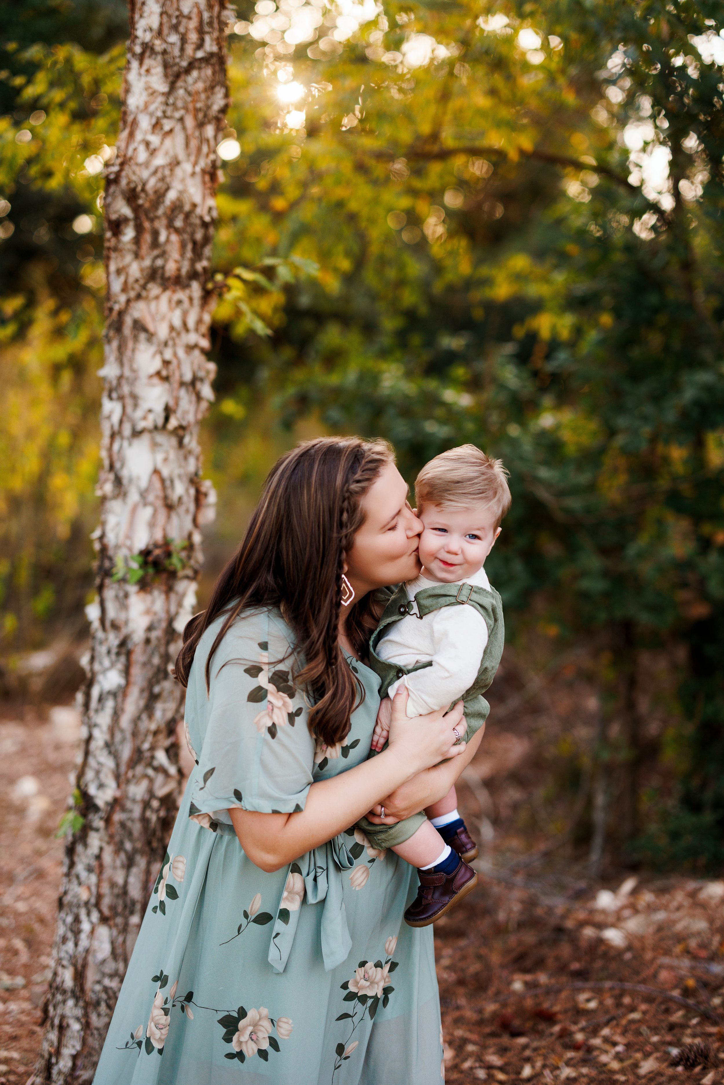 A tender moment captured in a wooded setting with autumn leaves and birch trees in the background.
