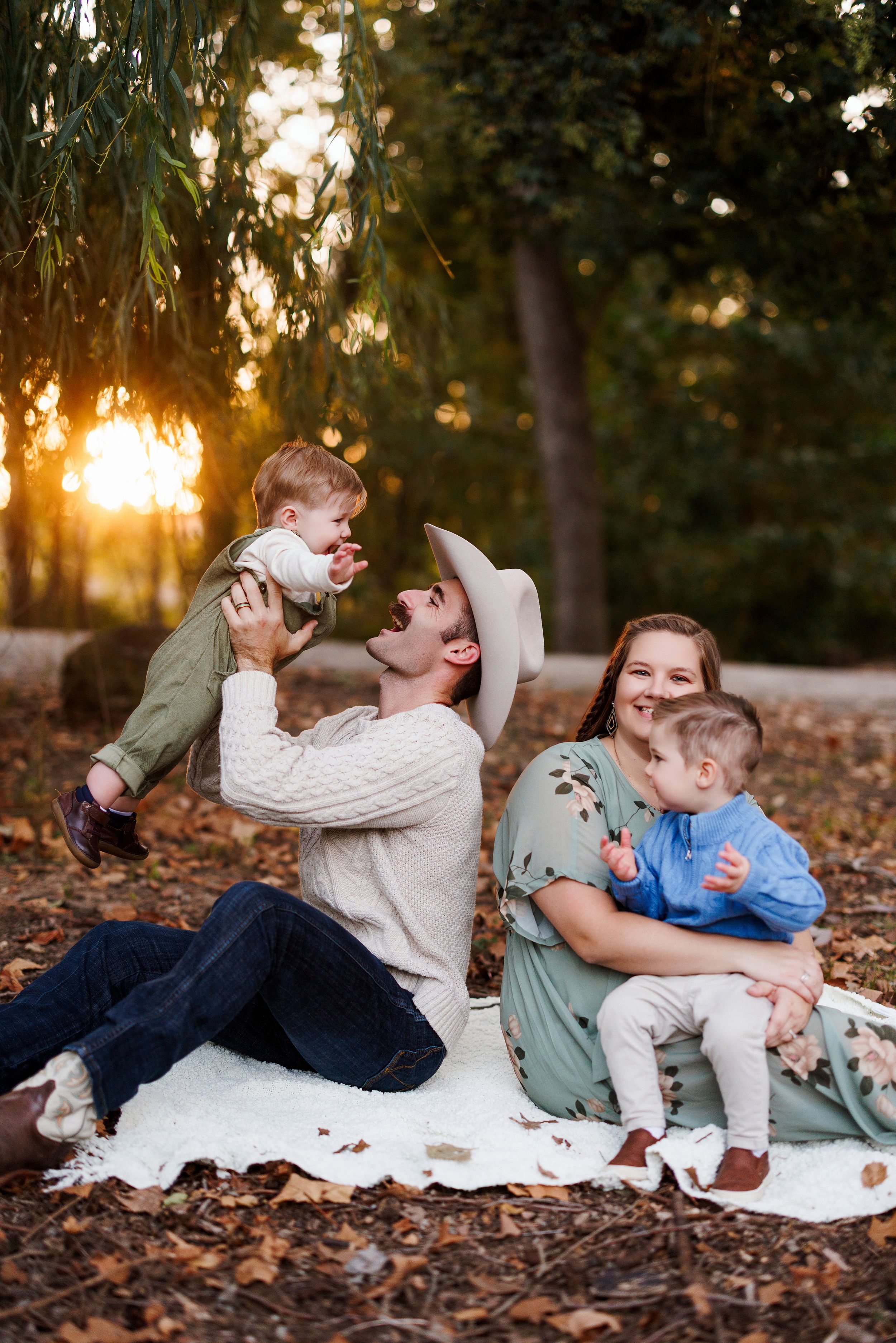 A family lying together on a white blanket in autumn leaves during golden hour sunset.