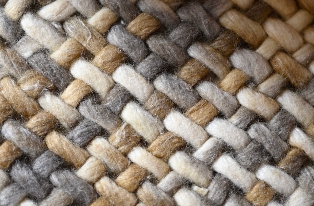 Close-up texture of woven beige and gray wool fabric showing intricate basket weave pattern detail.