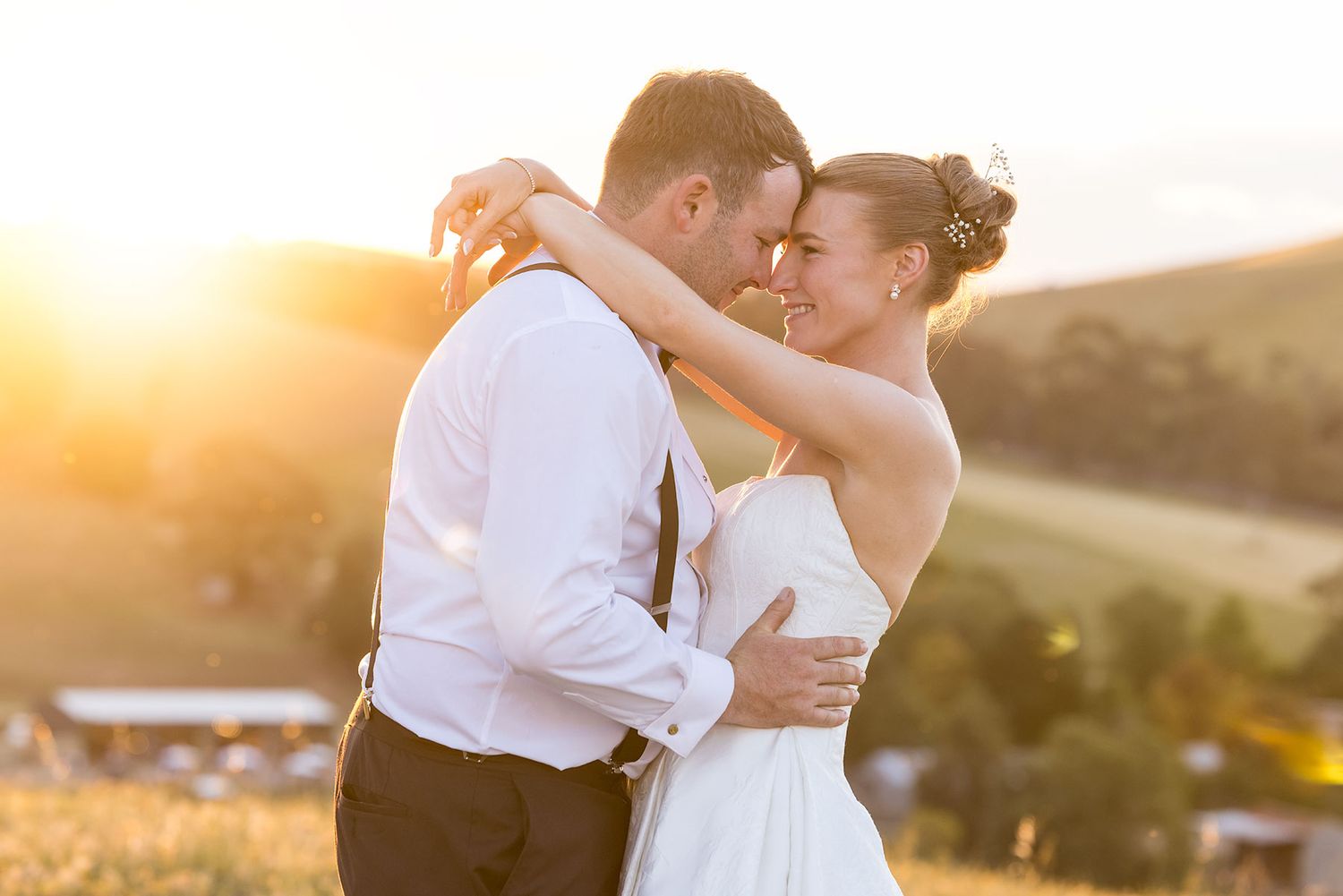 A couple shares romantic moments at sunset in their wedding attire against a golden glowing landscape.