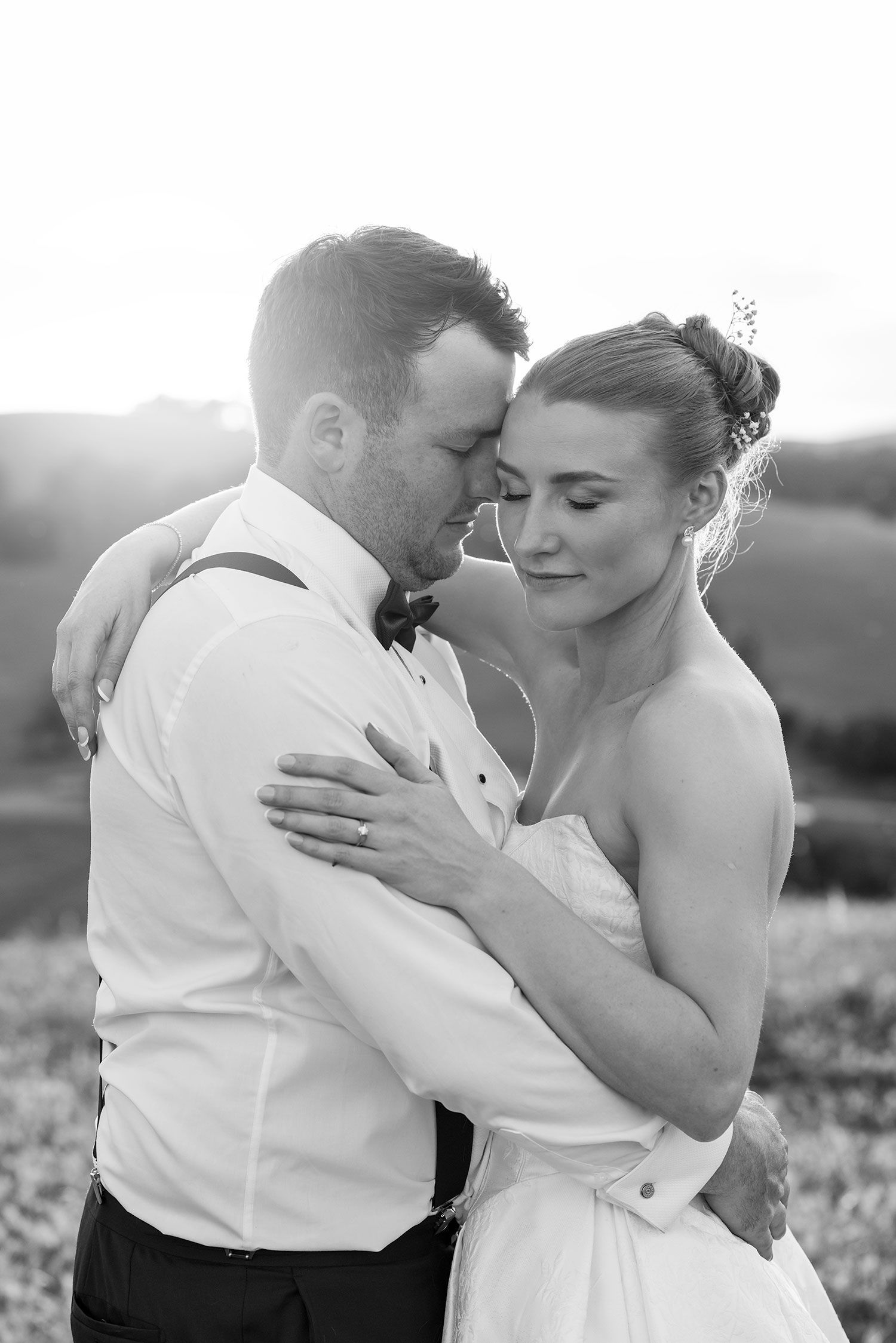 A romantic black and white wedding photo of a couple embracing in soft sunlight during their outdoor celebration.