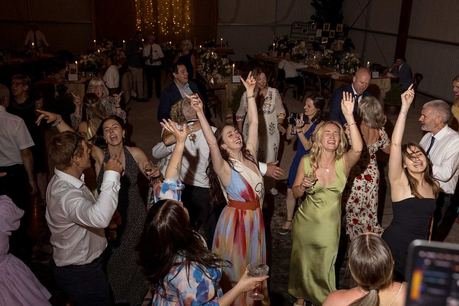 A large crowd of wedding guests dancing and celebrating together on a dance floor during an evening reception.