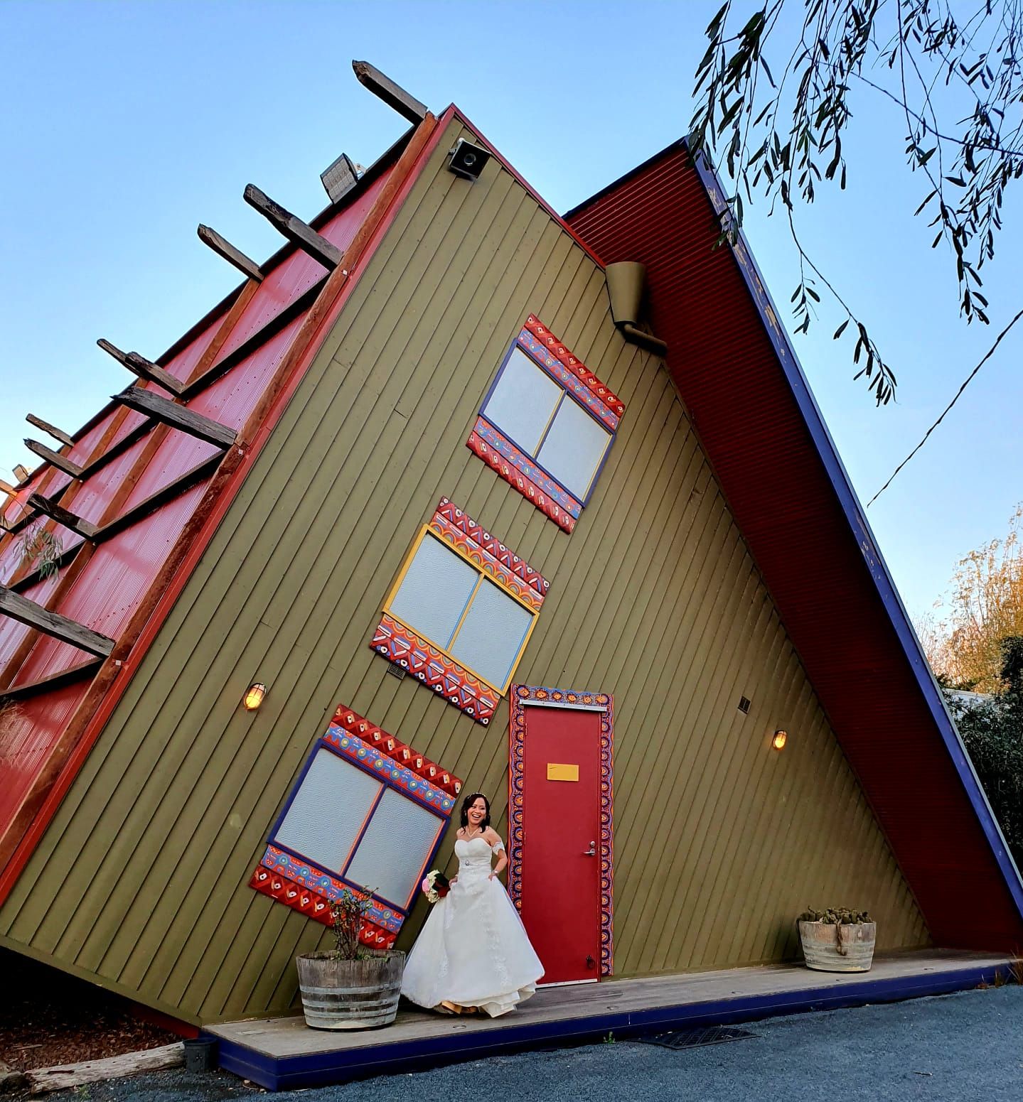 A unique A-frame building with red trim serves as backdrop for wedding photos.