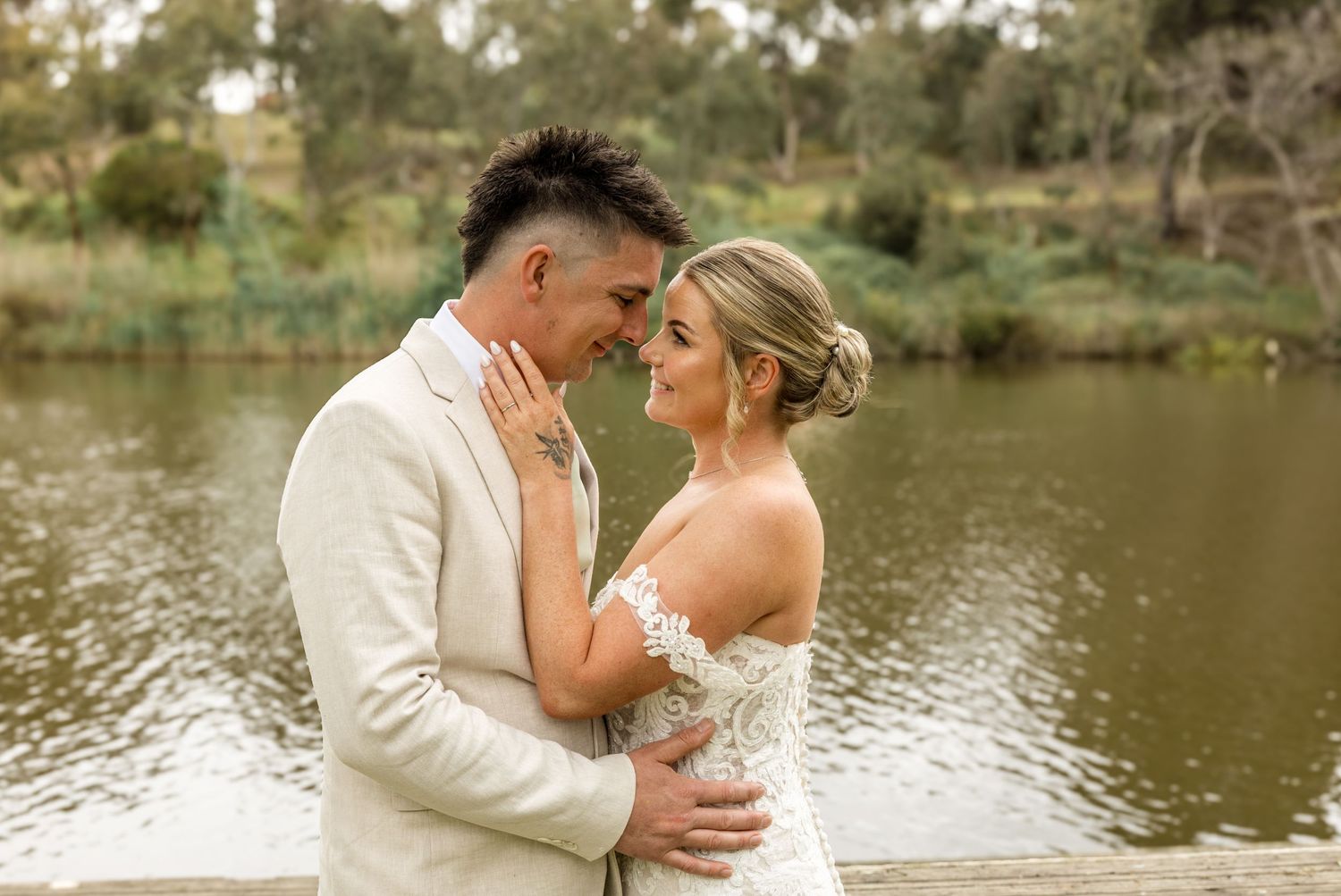 A romantic lakeside moment between newlyweds in light-colored wedding attire.