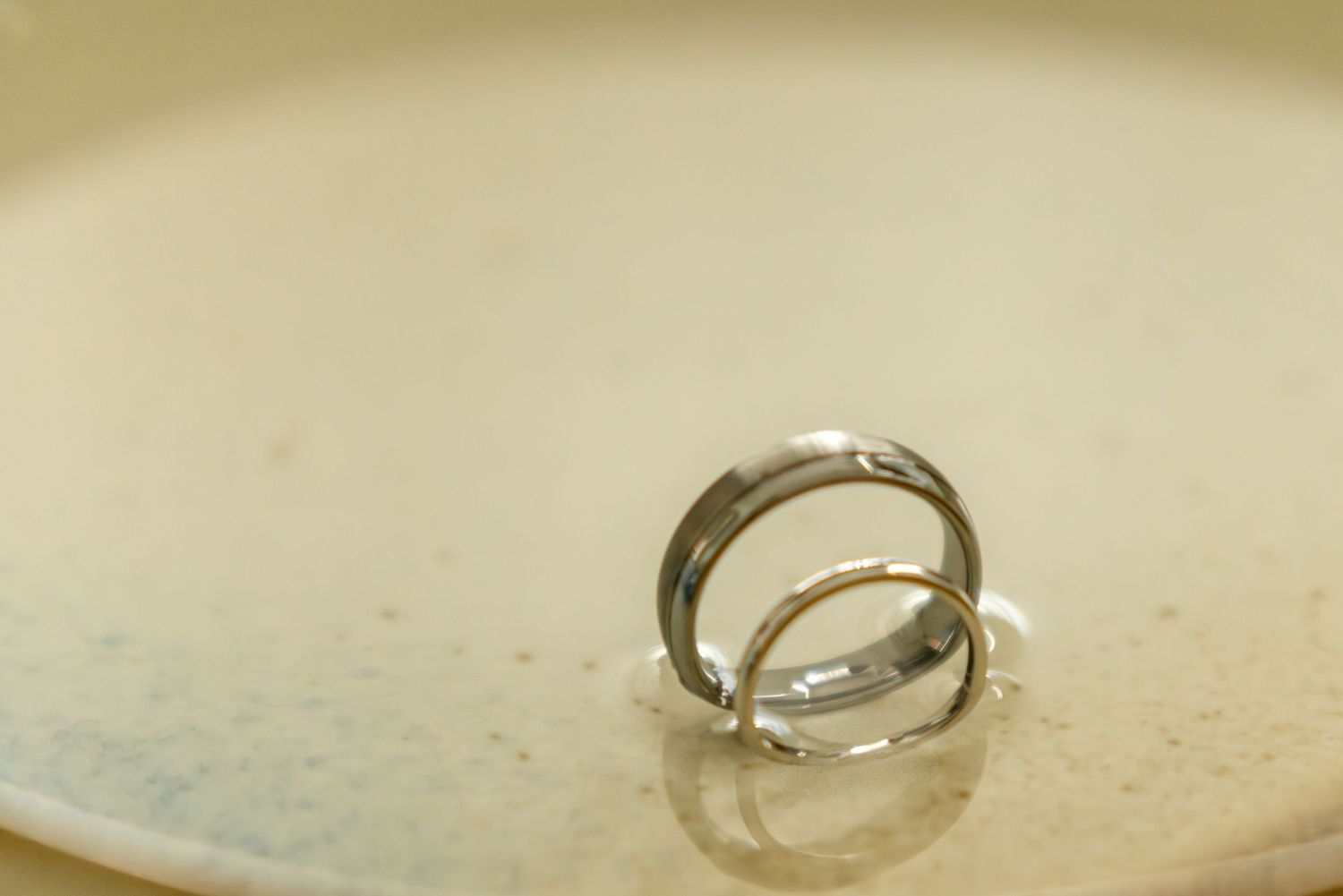 Two silver wedding rings photographed on a textured beige surface.