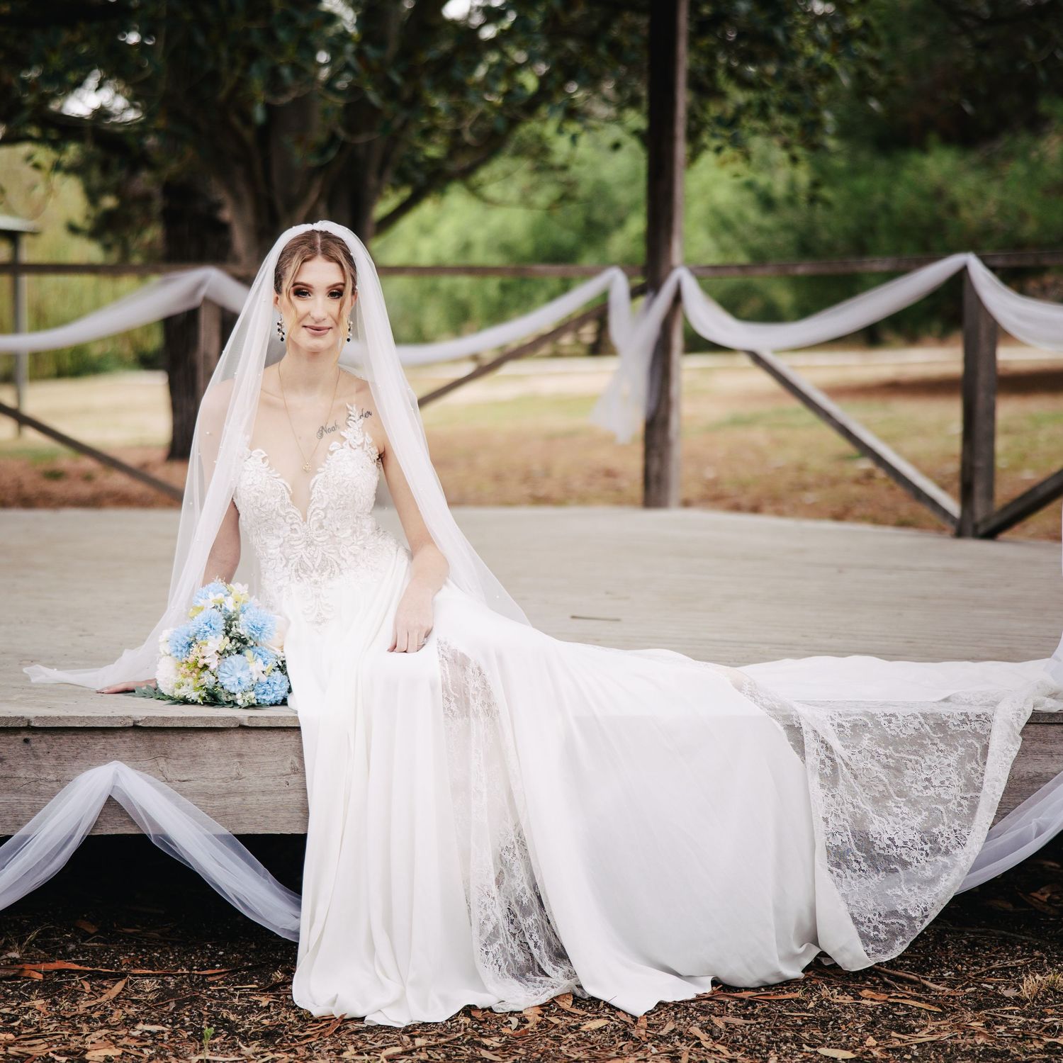 A bride in a lace wedding gown sits elegantly with her bouquet and flowing veil.