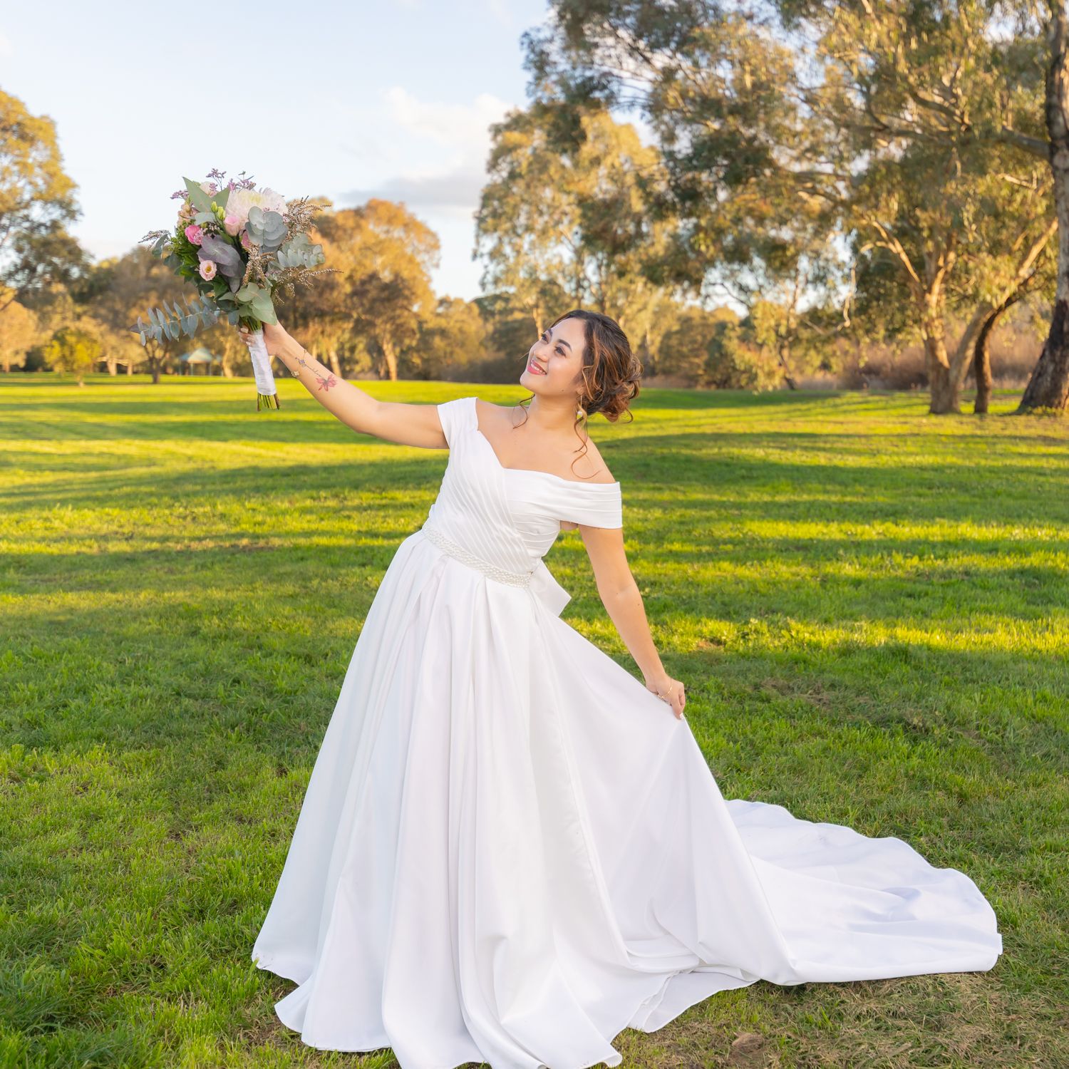 A white wedding dress billows in the breeze against a green field at sunset.