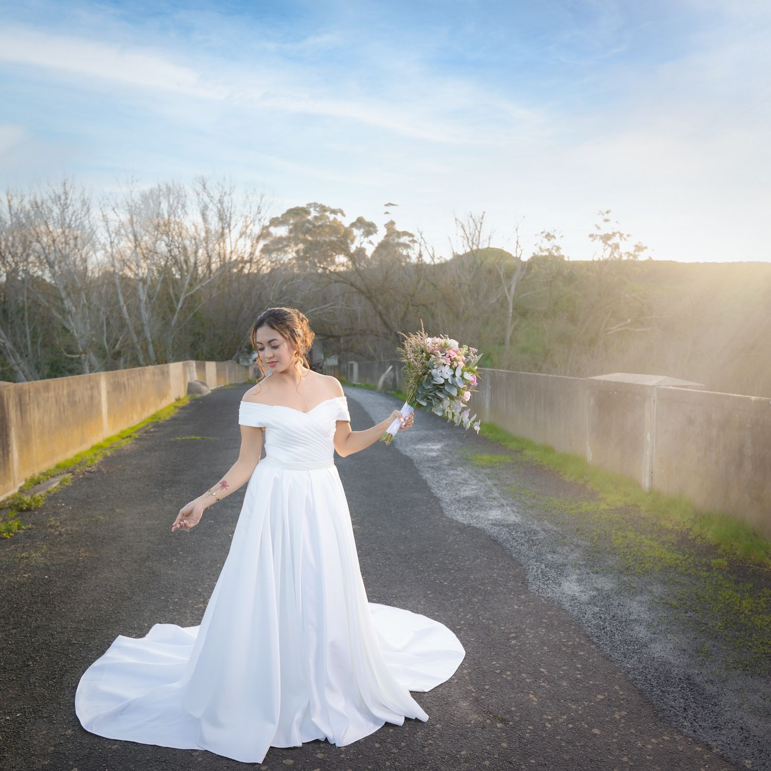 A bride in a flowing white gown spins joyfully on a gravel path.