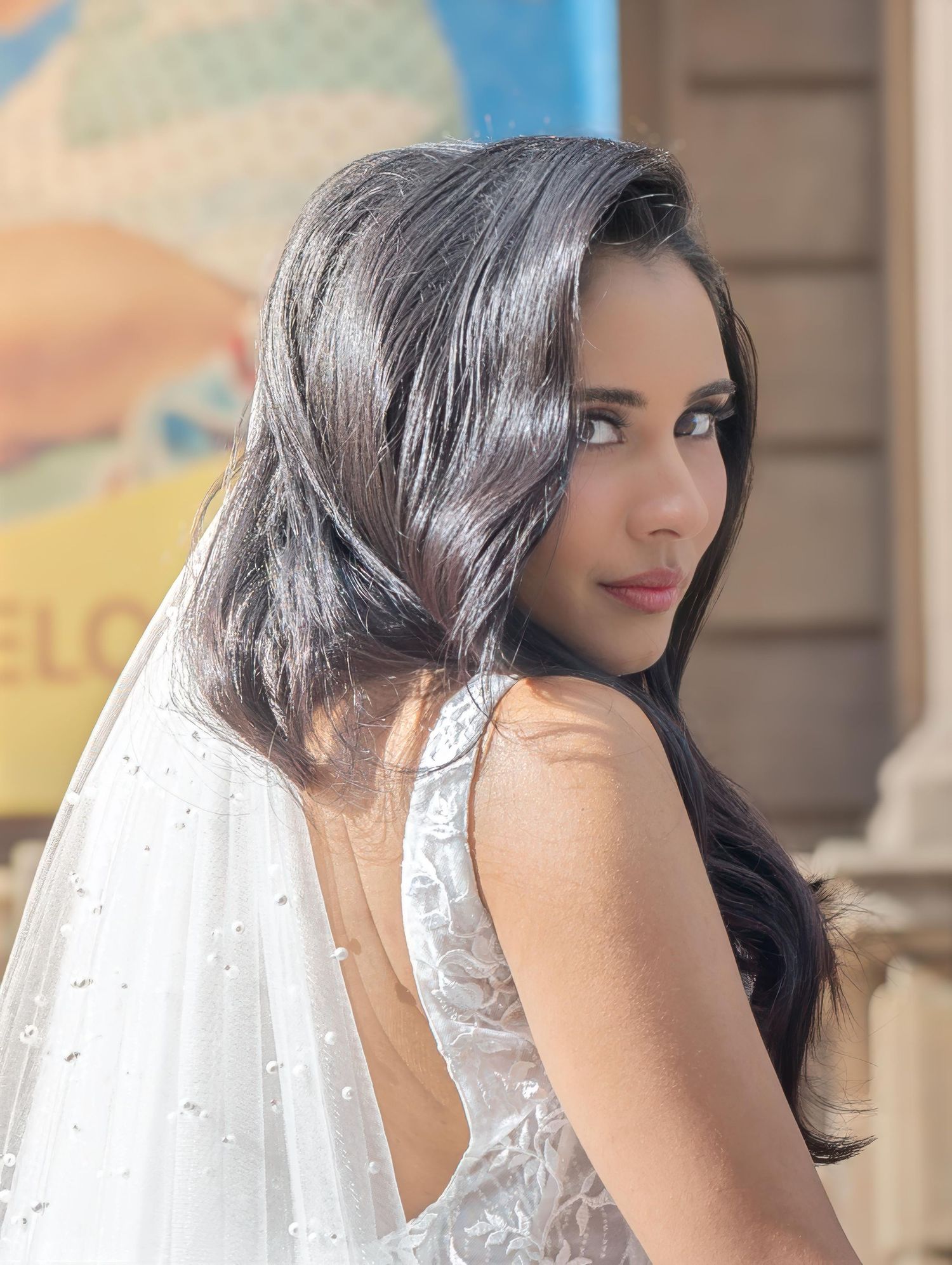 A bride in a sparkly white dress with long dark hair looks over her shoulder.