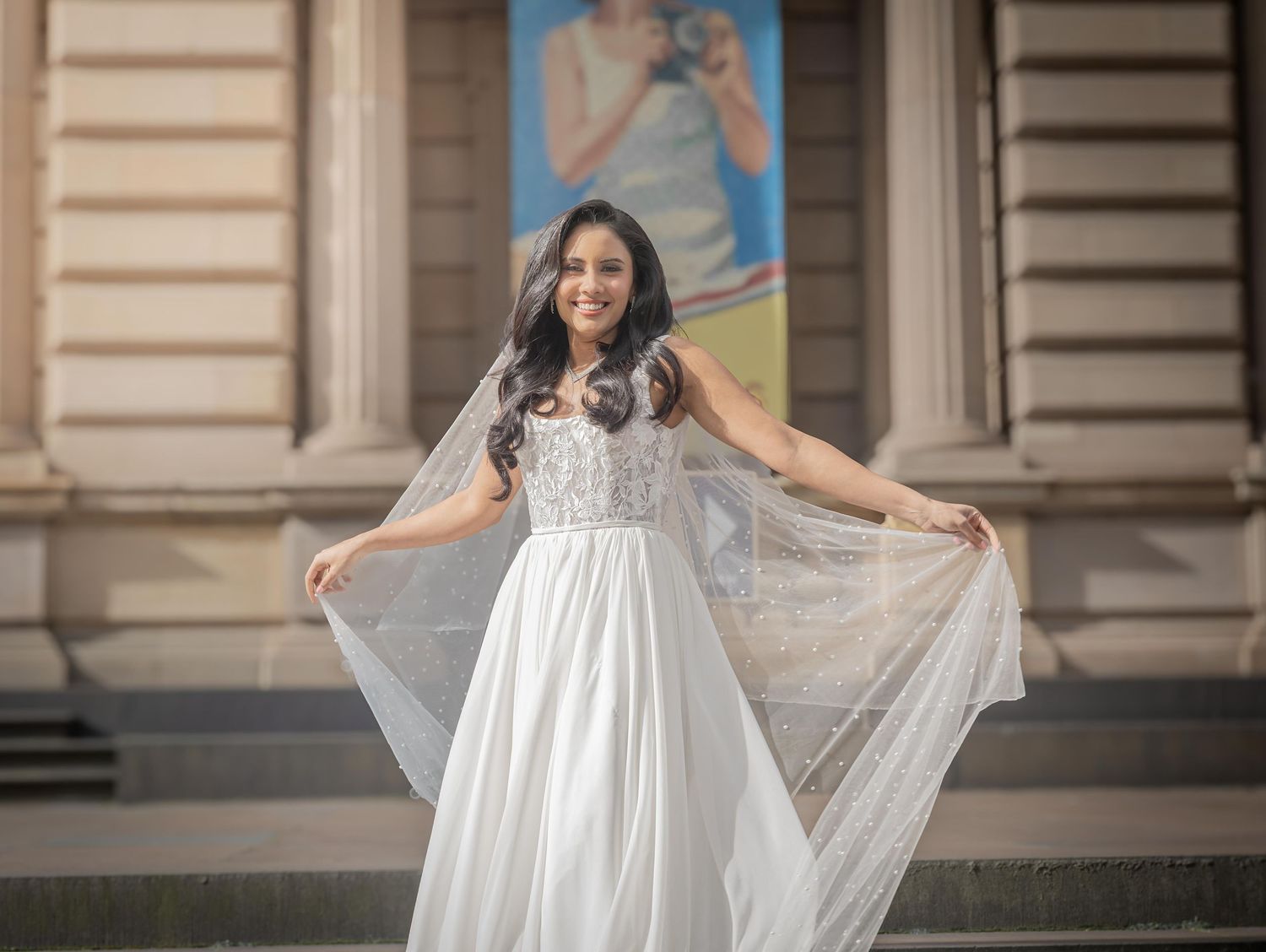 A person in a flowing white wedding dress poses elegantly on stone steps of a historic building.