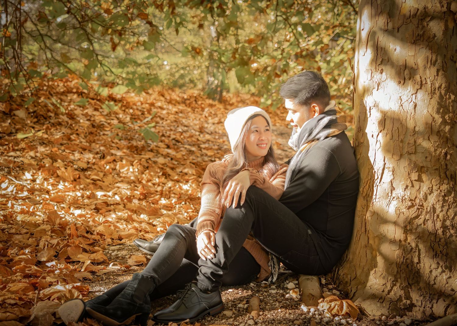 A couple sits among fallen autumn leaves during an outdoor photo session.