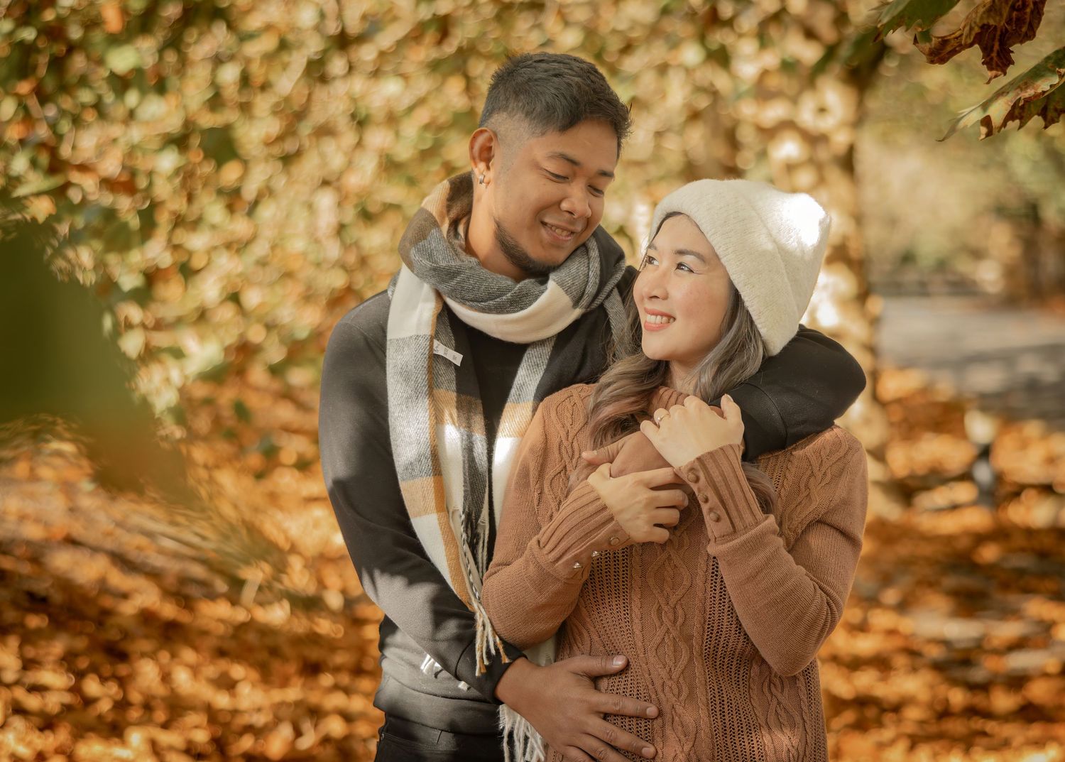 A joyful couple sharing a tender moment outdoors in autumn wearing cozy winter accessories.