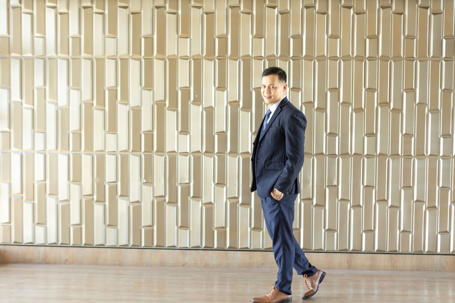 Groom in navy suit walking past modern geometric wall design.