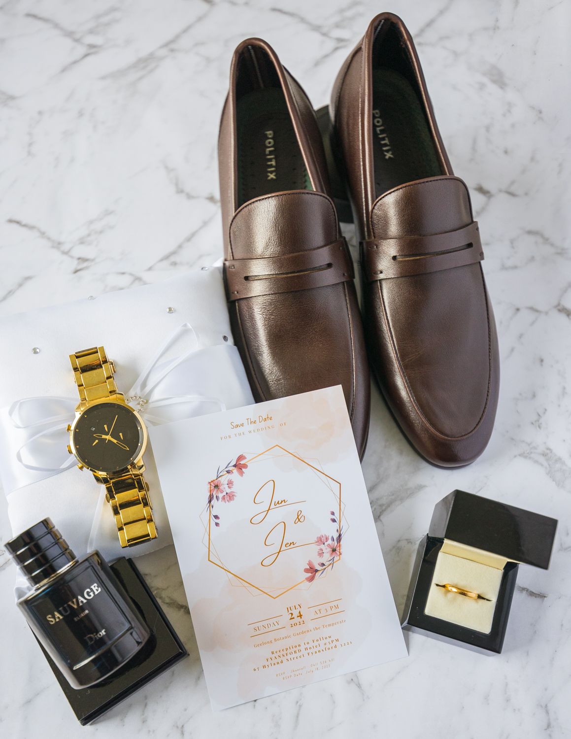 Brown leather loafers with gold watch and wedding invitation flatlay on marble surface.