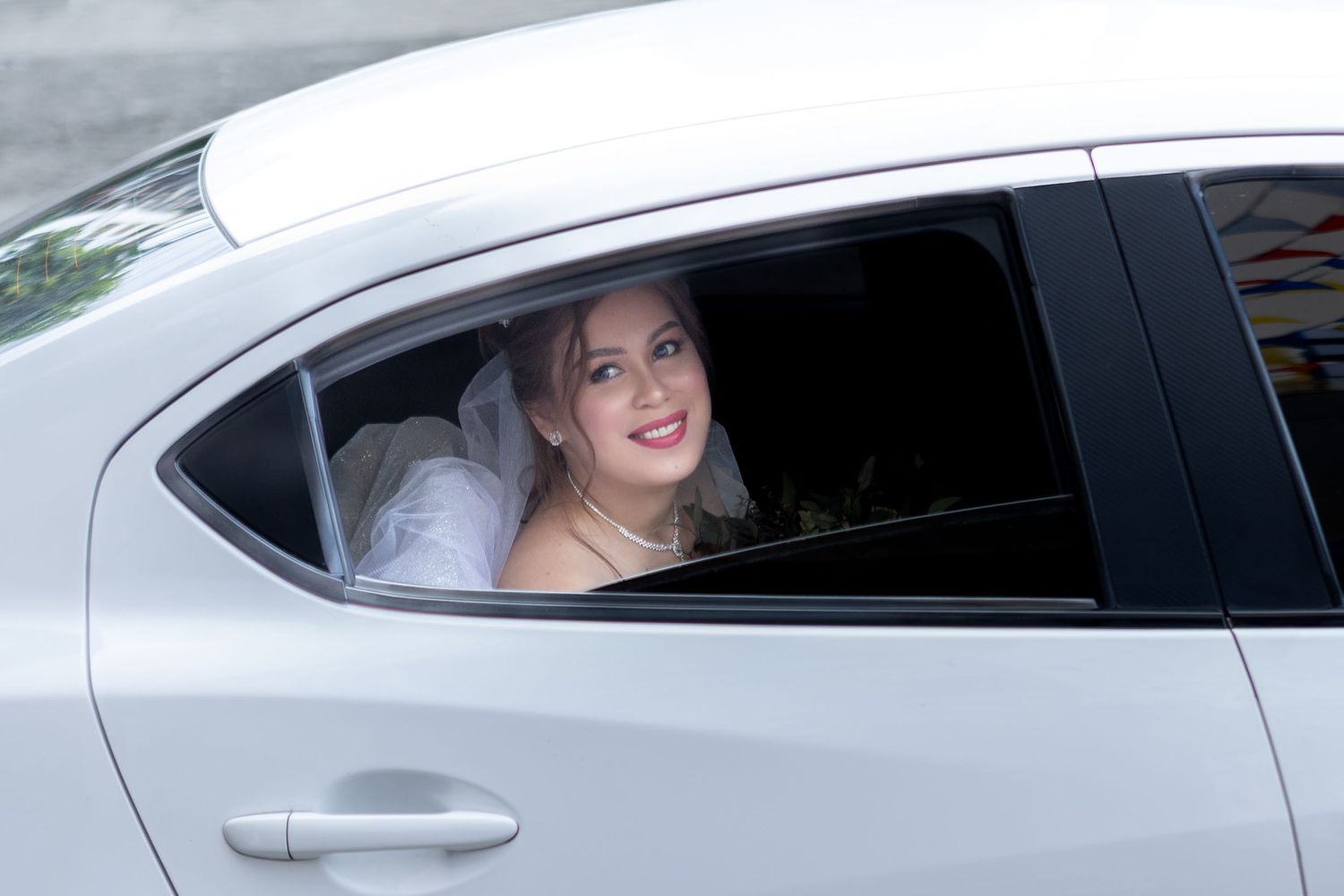 Joyful bride smiling through car window on wedding day.