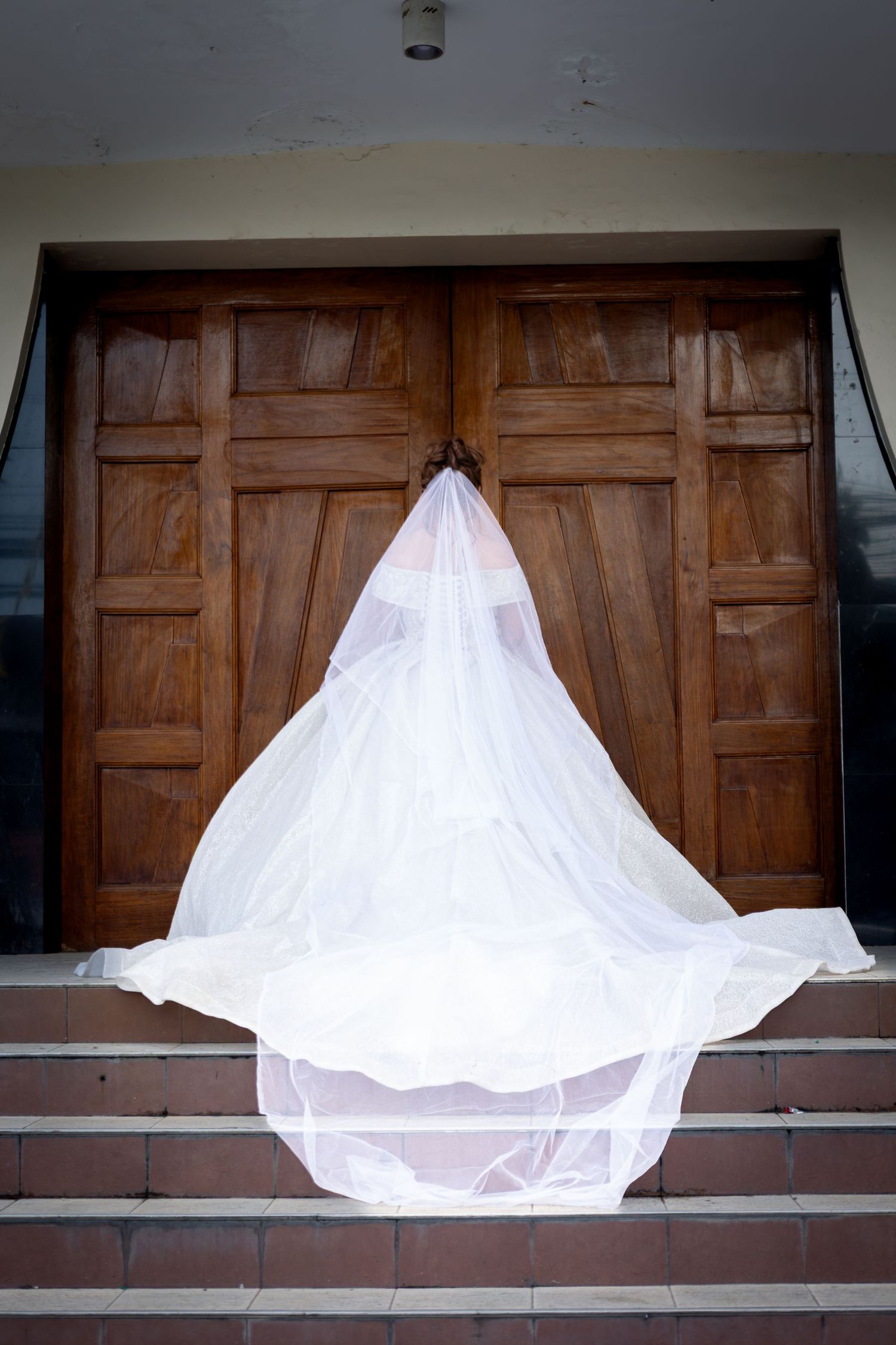 Dramatic cathedral-length wedding veil cascading down wooden church doors and steps.