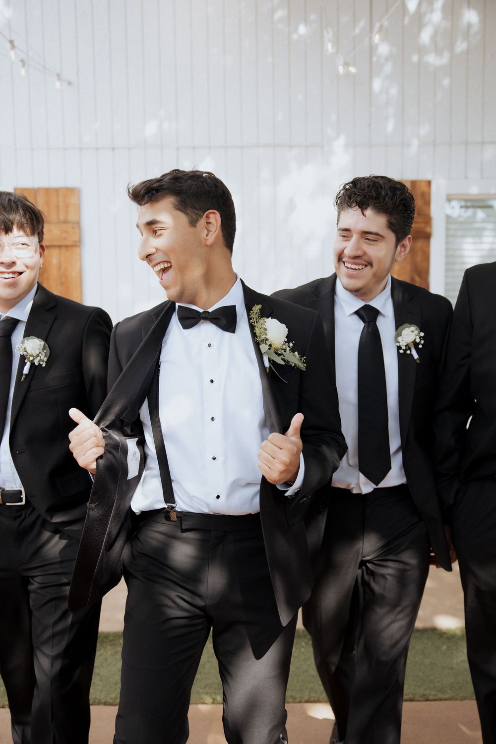 Groomsmen in black tuxedos and bow ties share a candid laughing moment together at a wedding.