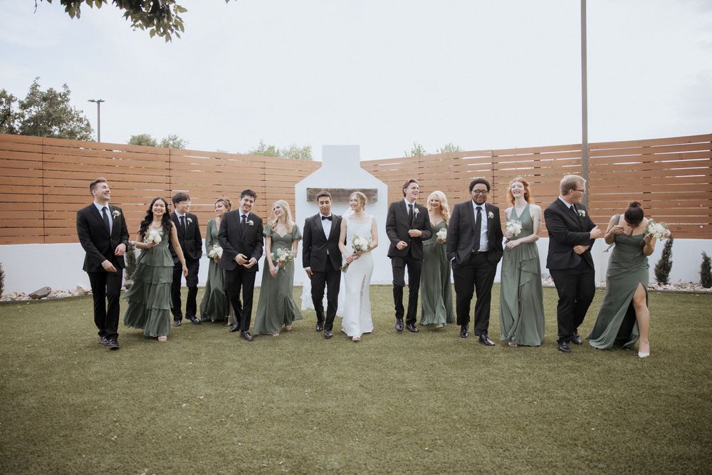 Wedding party members lined up outdoors for group photos at a scenic venue with wooden walls and grassy areas.