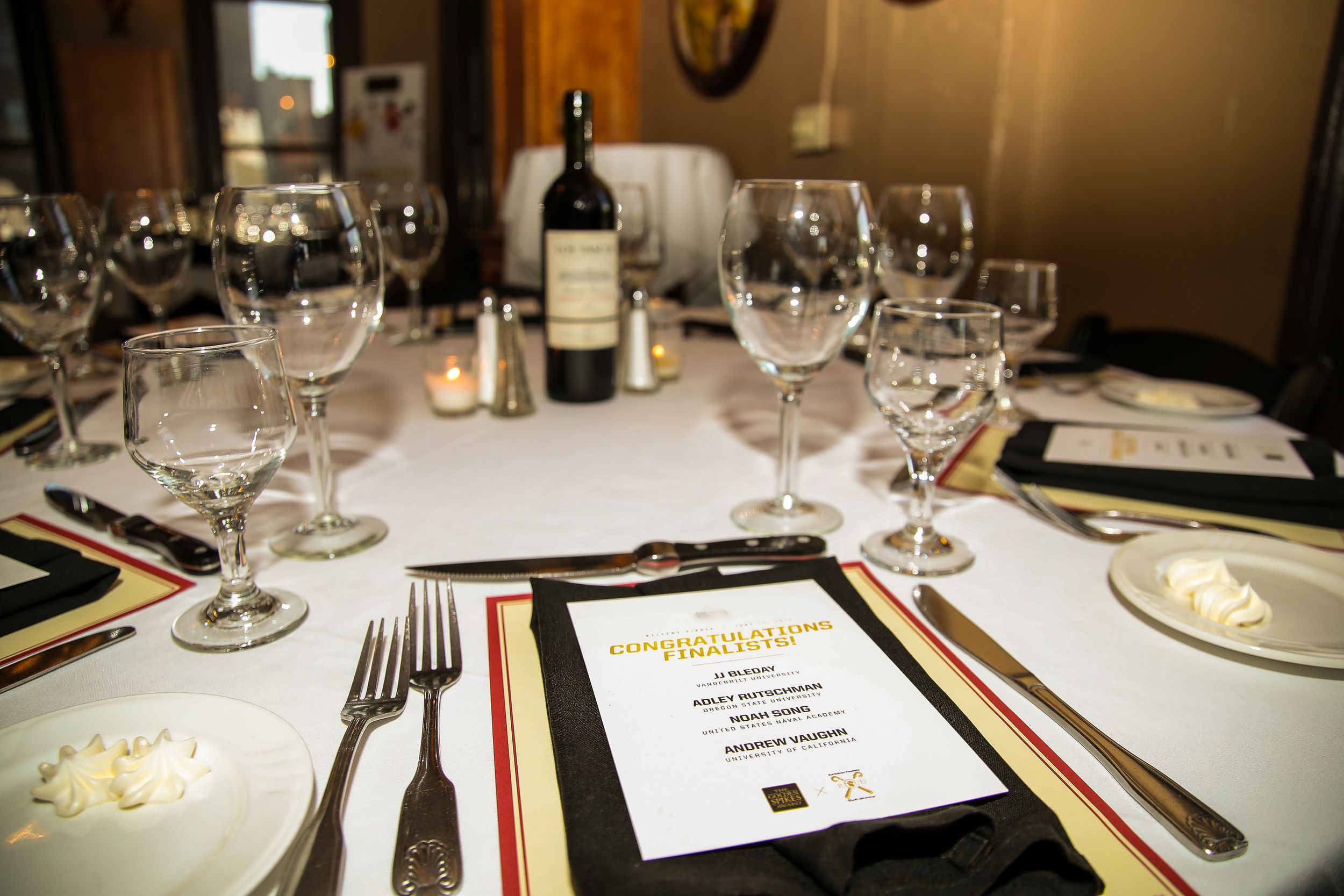 Elegant dinner table setting with wine glasses, silverware, candles and Golden Spikes Award menu cards.