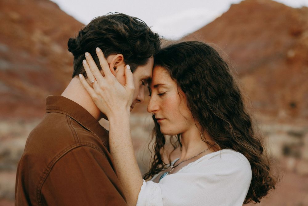 Intimate couple touching foreheads gently with red rock canyon softly blurred in background.