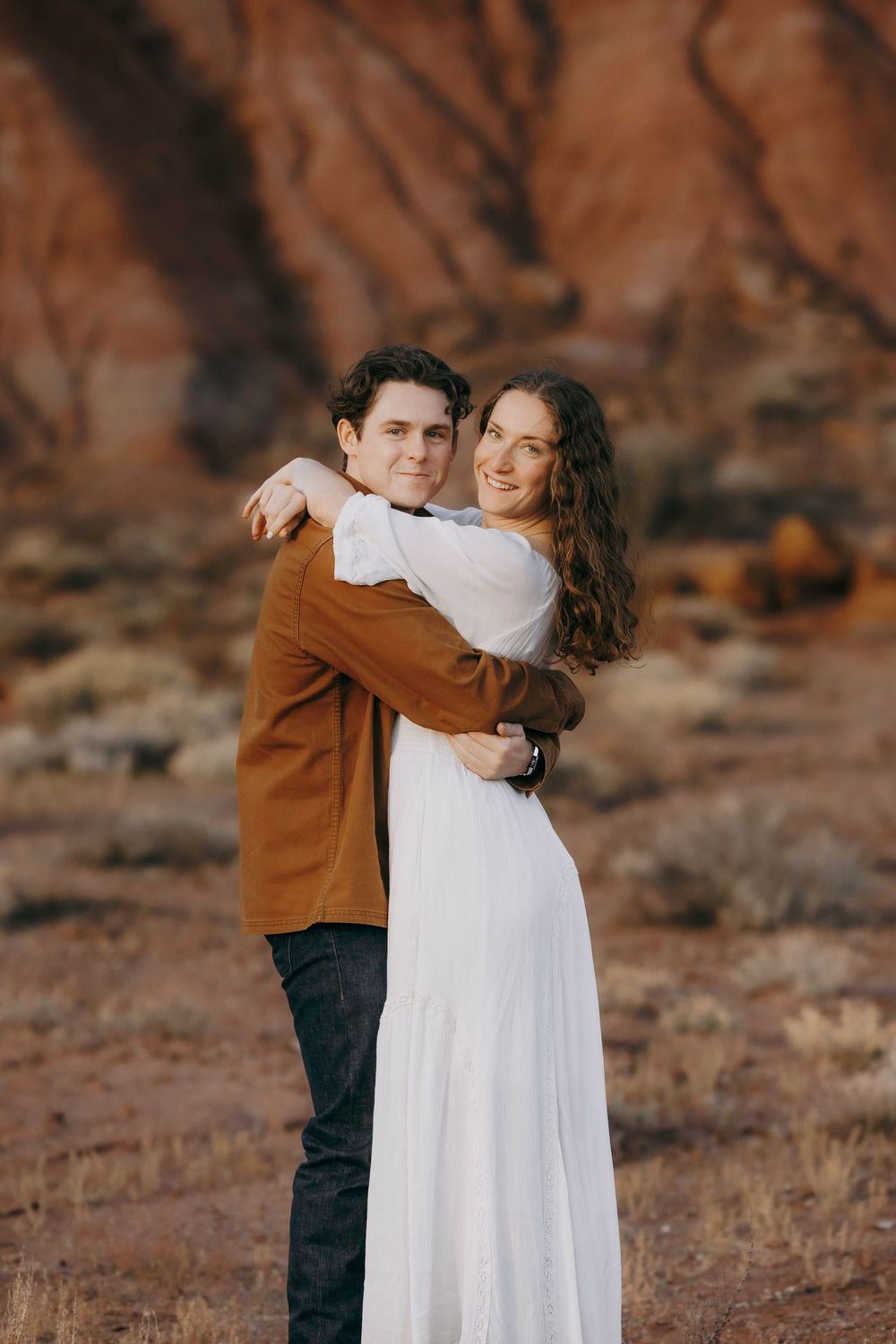 Couple embracing tenderly in front of stunning red rock canyon landscape at sunset.