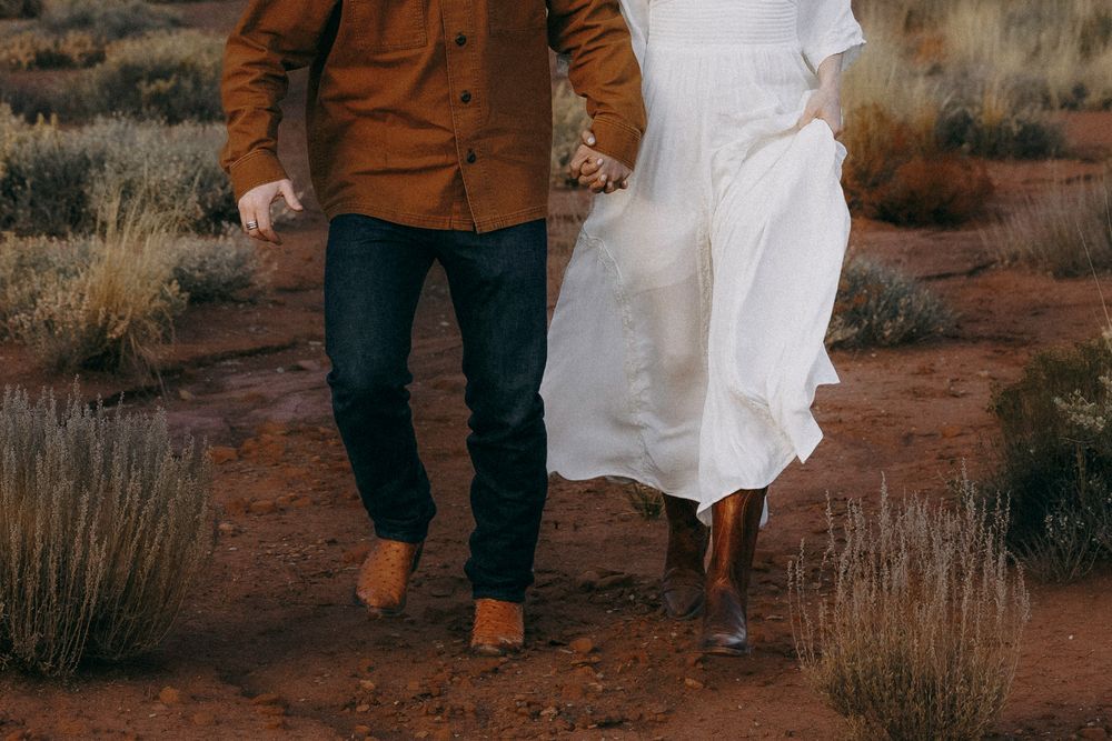 Close-up of couple holding hands while walking on red desert soil path together.