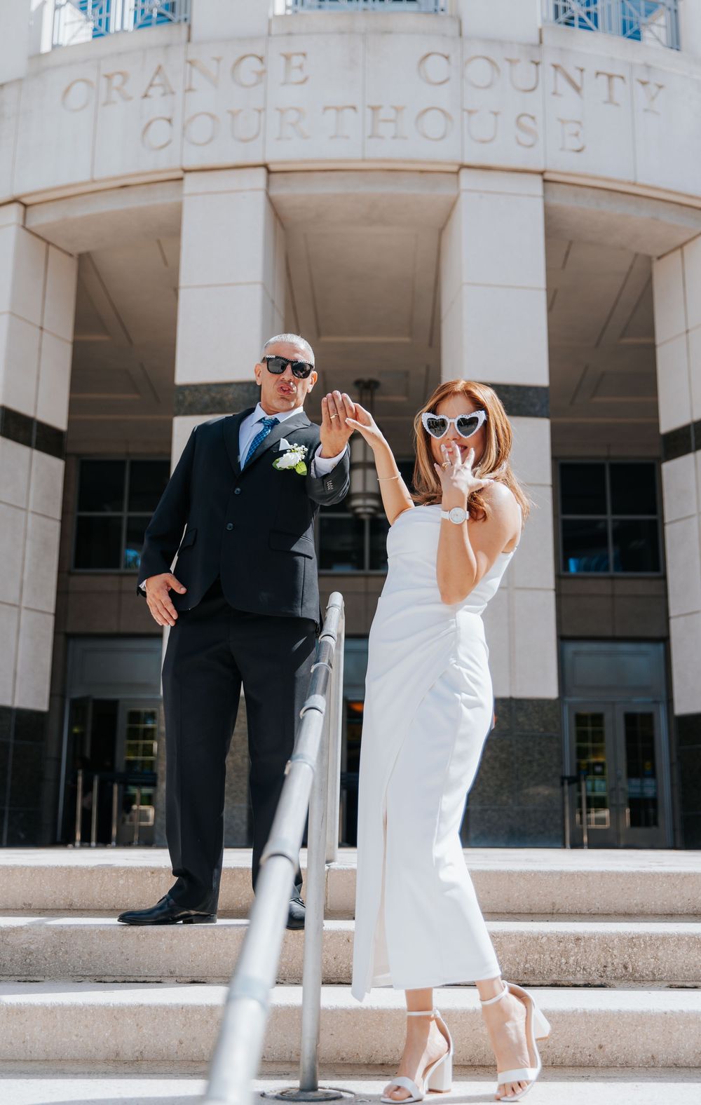 Stylish couple in sunglasses posing outside a building with white columns.