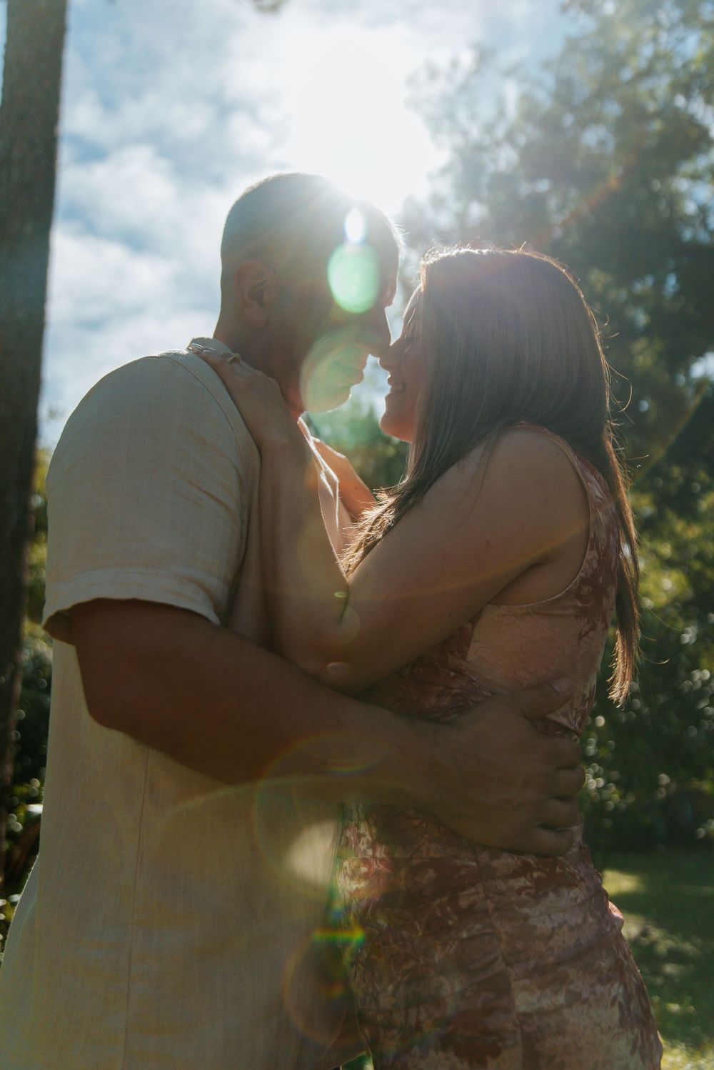 A romantic embrace with sunlight streaming through trees.