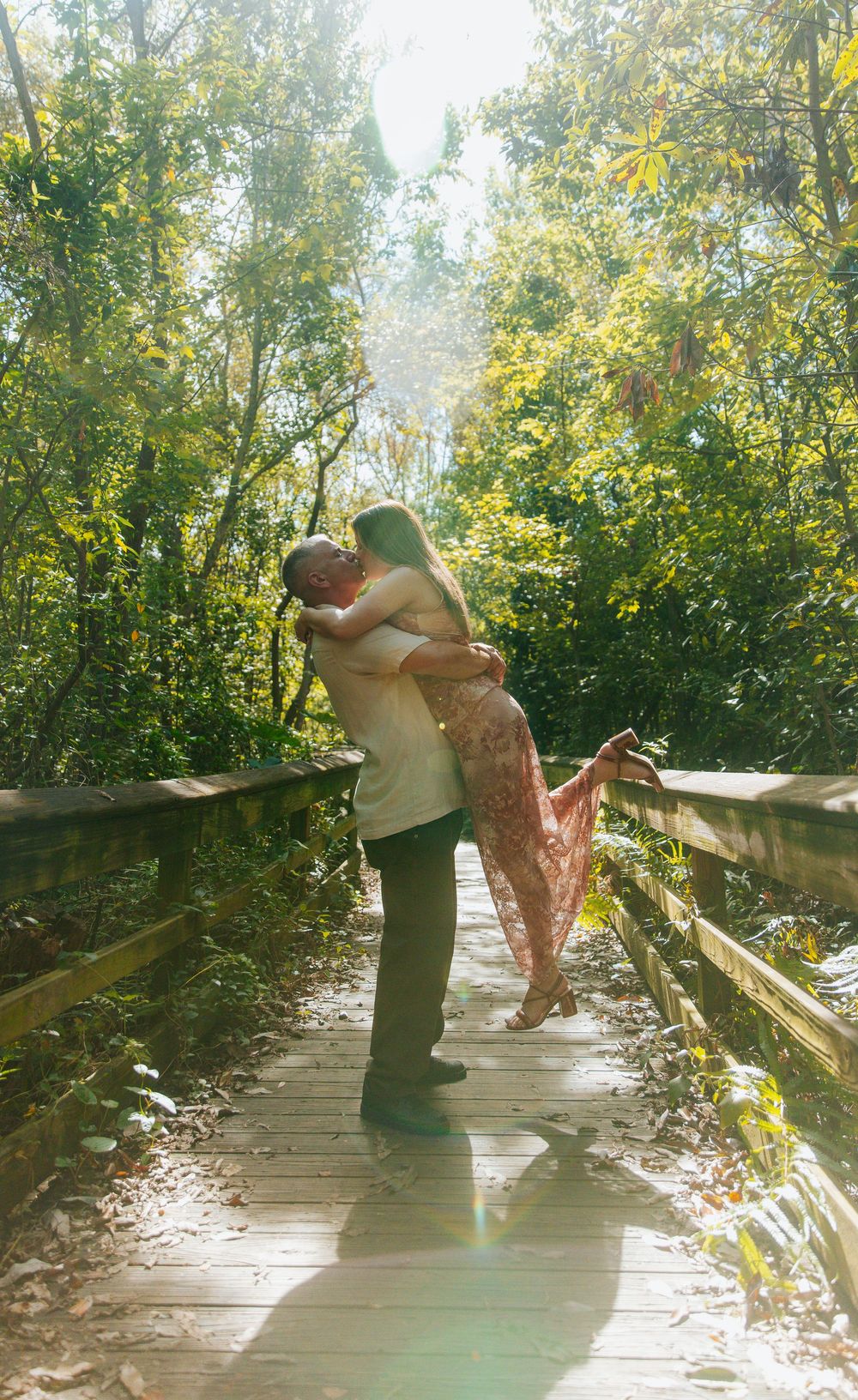 A romantic lift pose on a wooden boardwalk surrounded by lush greenery.