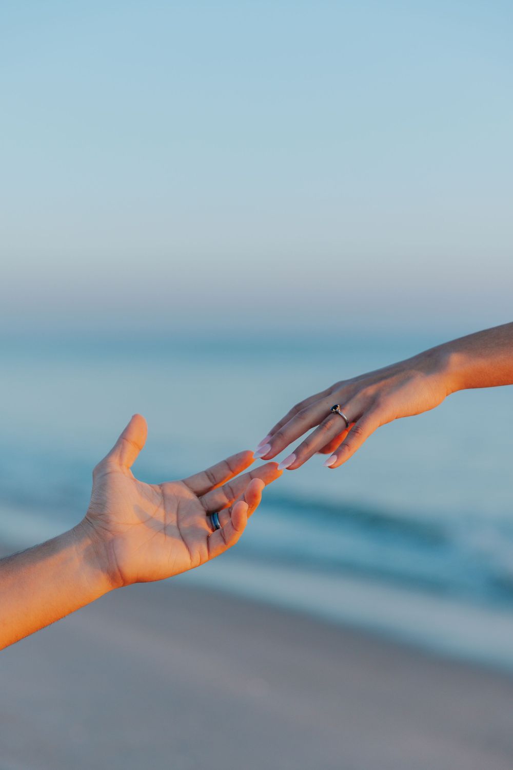 Two hands reaching toward each other against a blurred ocean background.