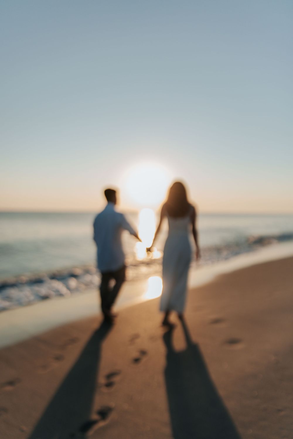 Blurred silhouettes walking on beach at sunset leaving footprints in sand.