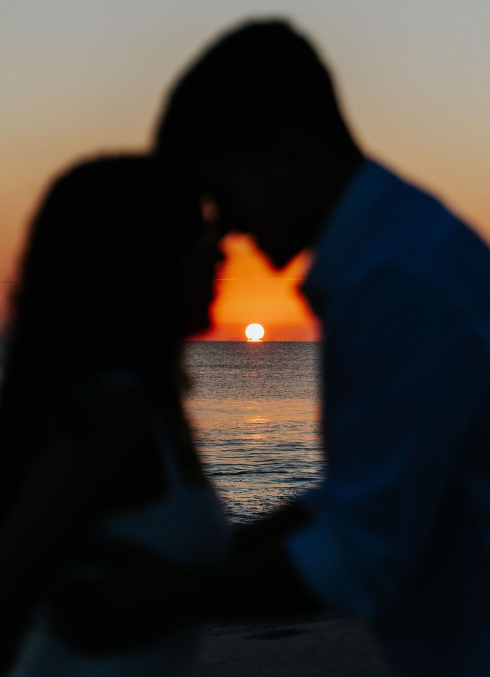 Silhouetted couple against an orange sunset over ocean waters.