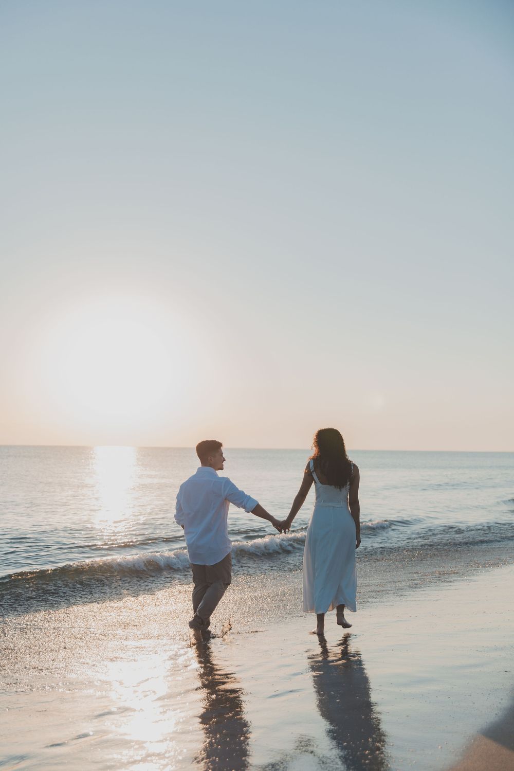 Couple walking in shallow ocean water during sunset with golden light reflections.