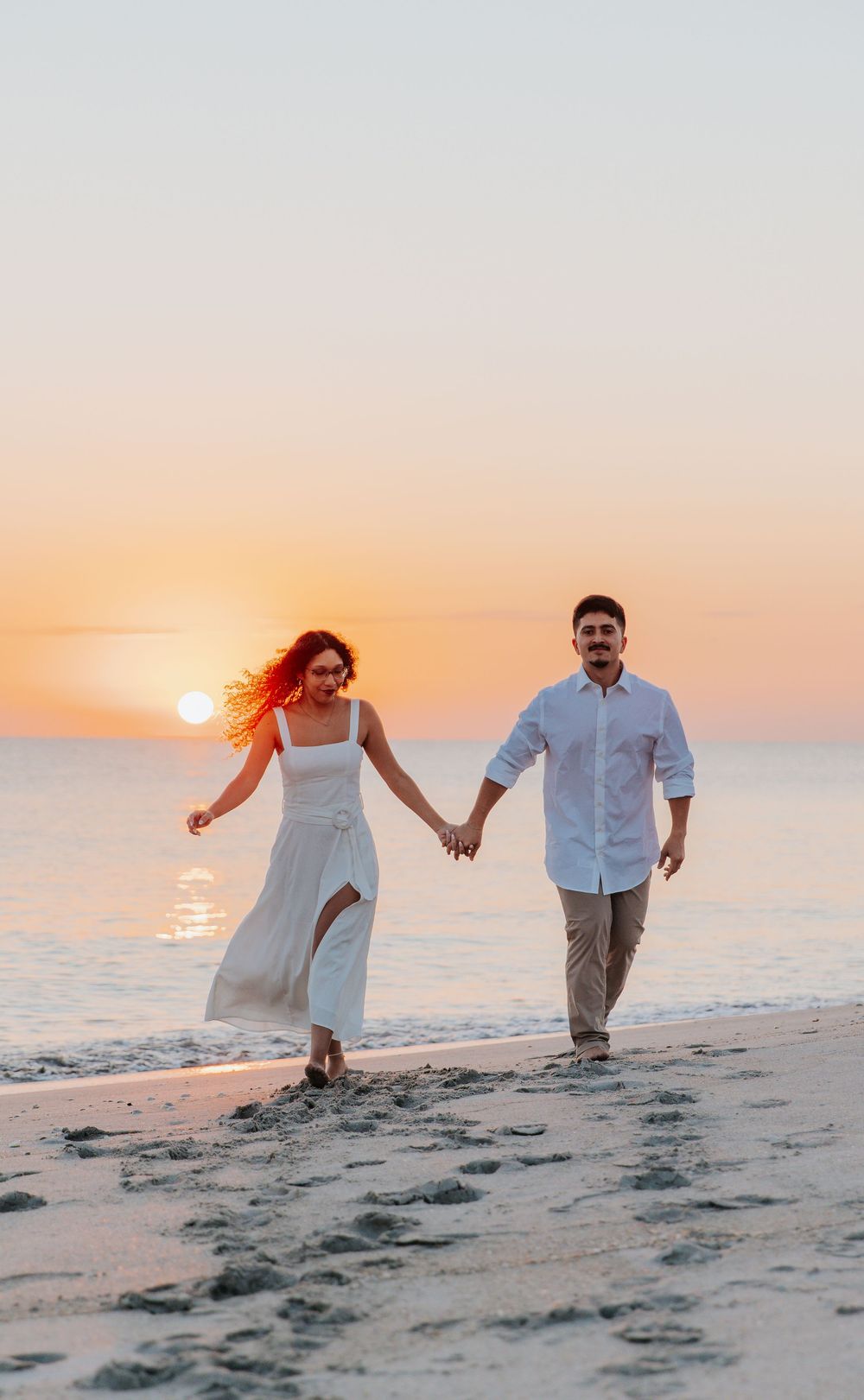 Couple walking hand in hand on beach during golden hour sunset.
