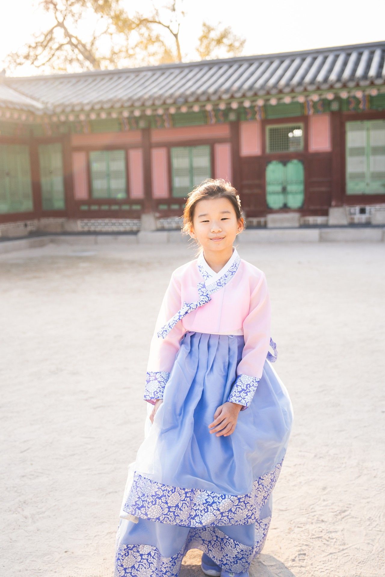 Traditional Korean hanbok dress in blue and pink shown in outdoor courtyard setting with traditional architecture.