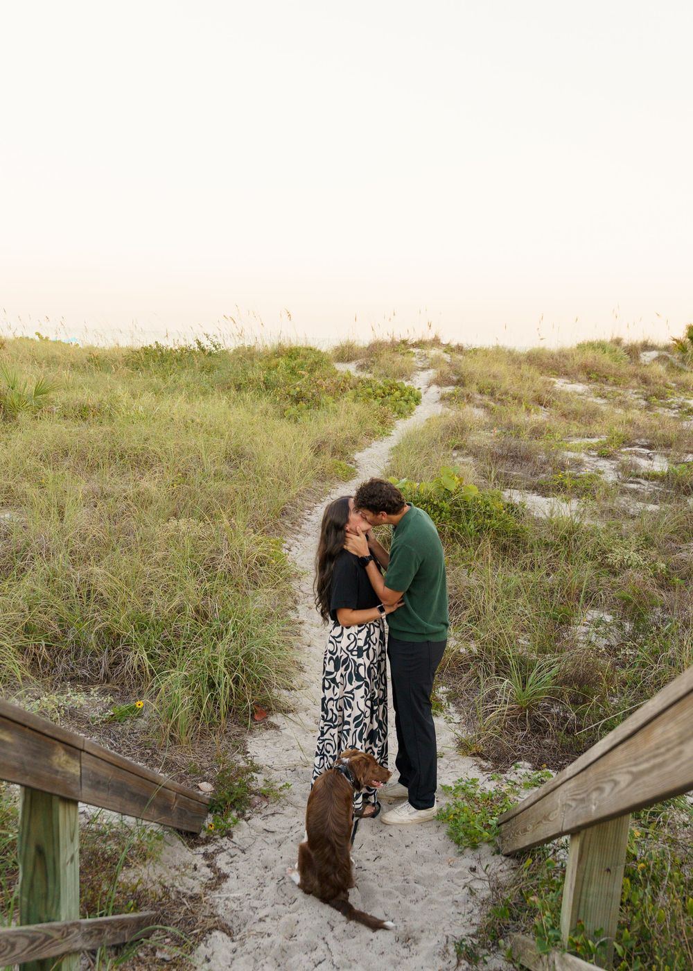 A couple shares an intimate moment together on a sandy beach boardwalk during sunset.