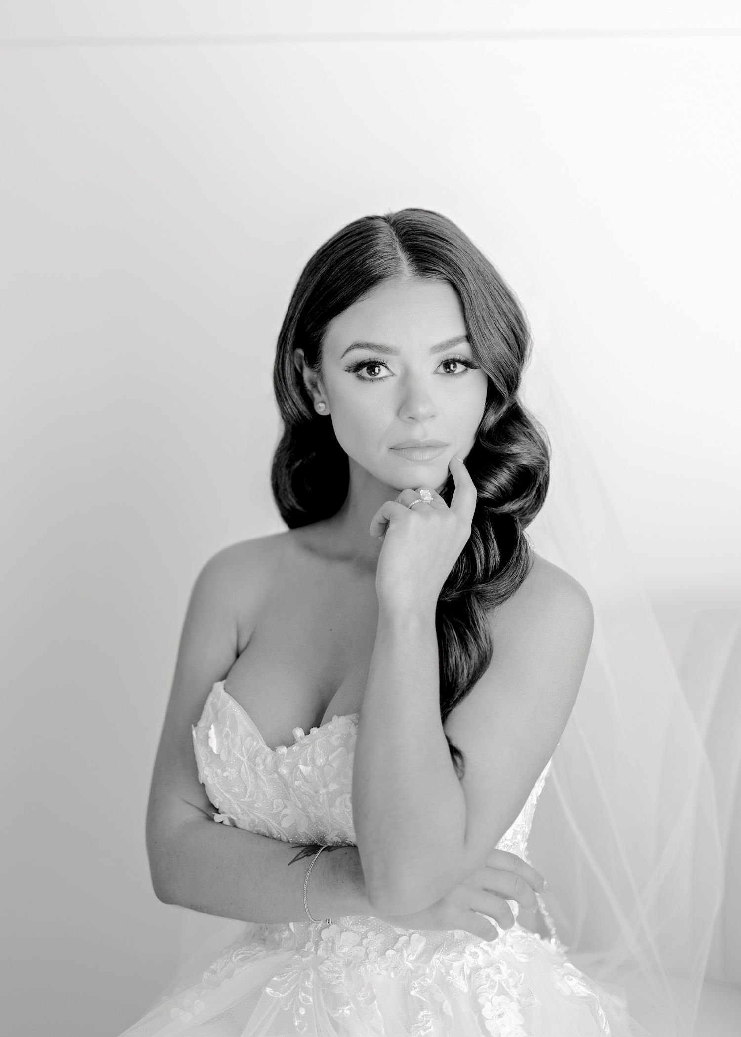 Black and white portrait of someone in a strapless lace wedding gown with long dark hair styled in soft waves.