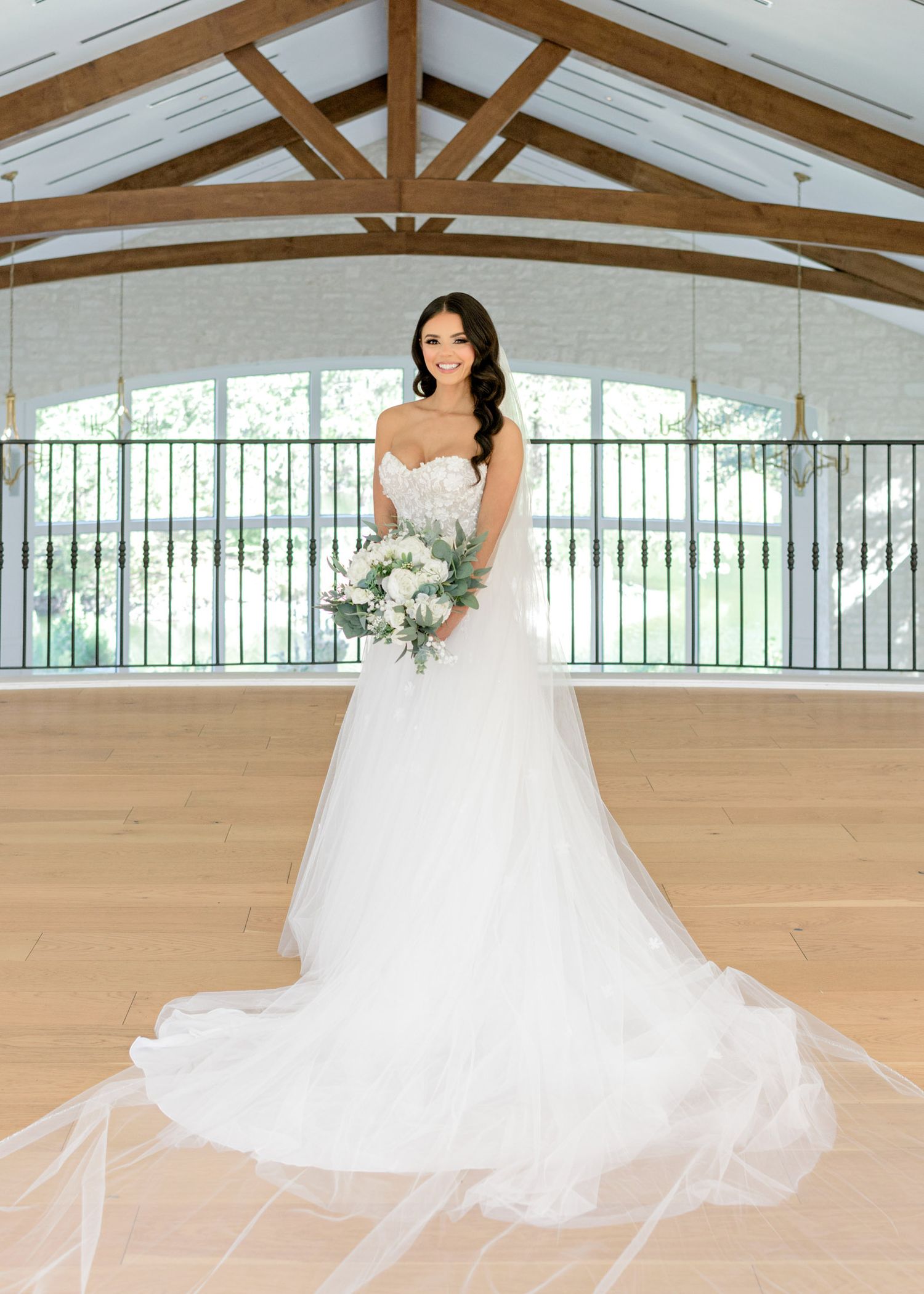 A flowing white wedding dress twirls elegantly across a light wooden floor in a bright venue with exposed beams.