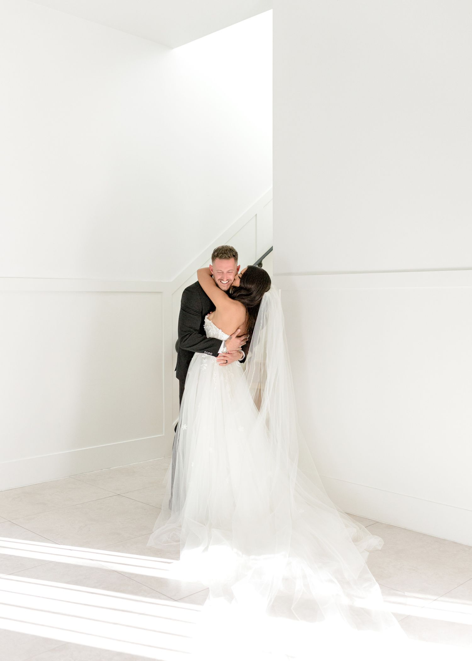 Romantic wedding couple shares intimate kisses in an elegant white studio setting.