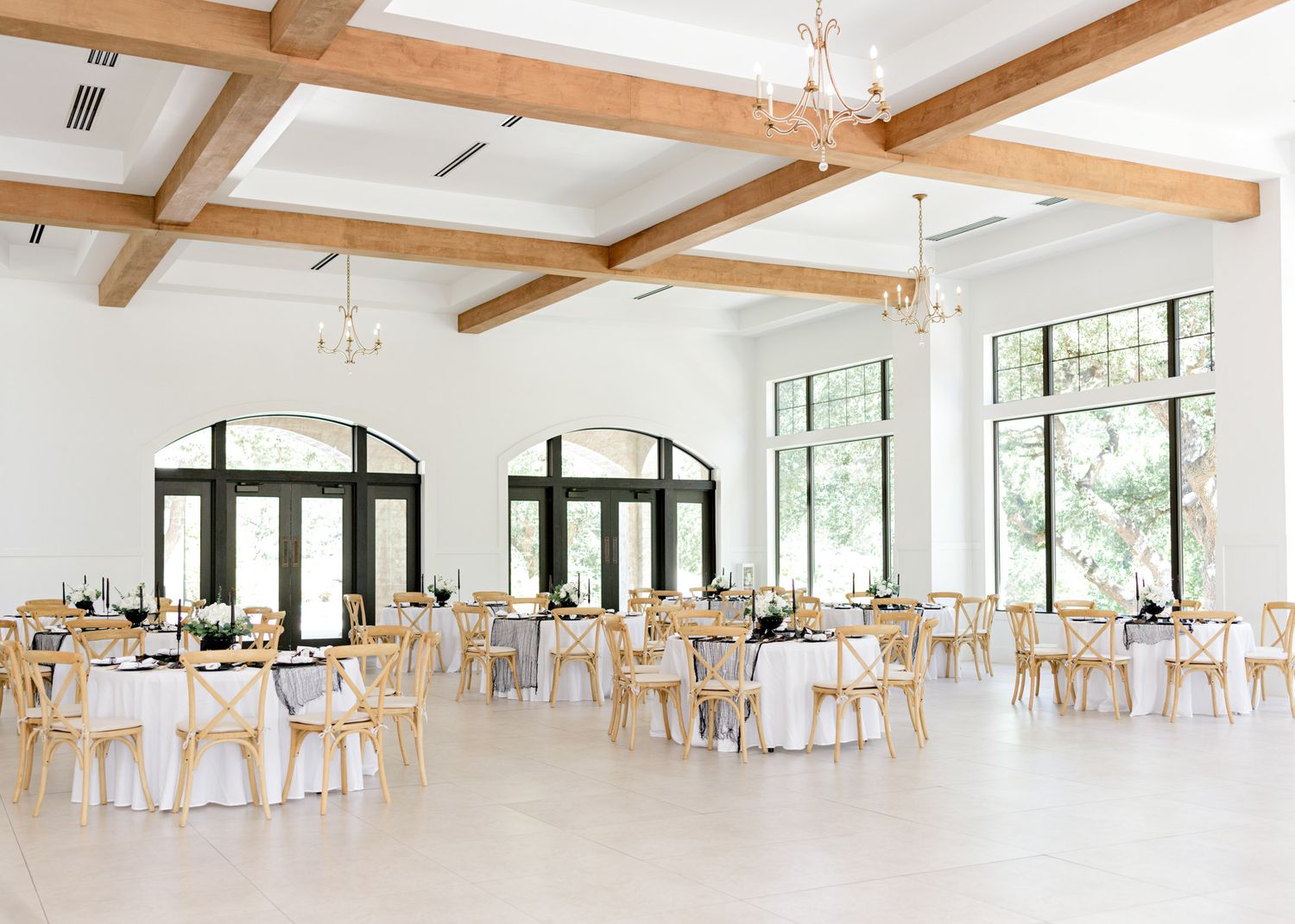 Modern white wedding reception venue with exposed wooden beams and elegant table settings.