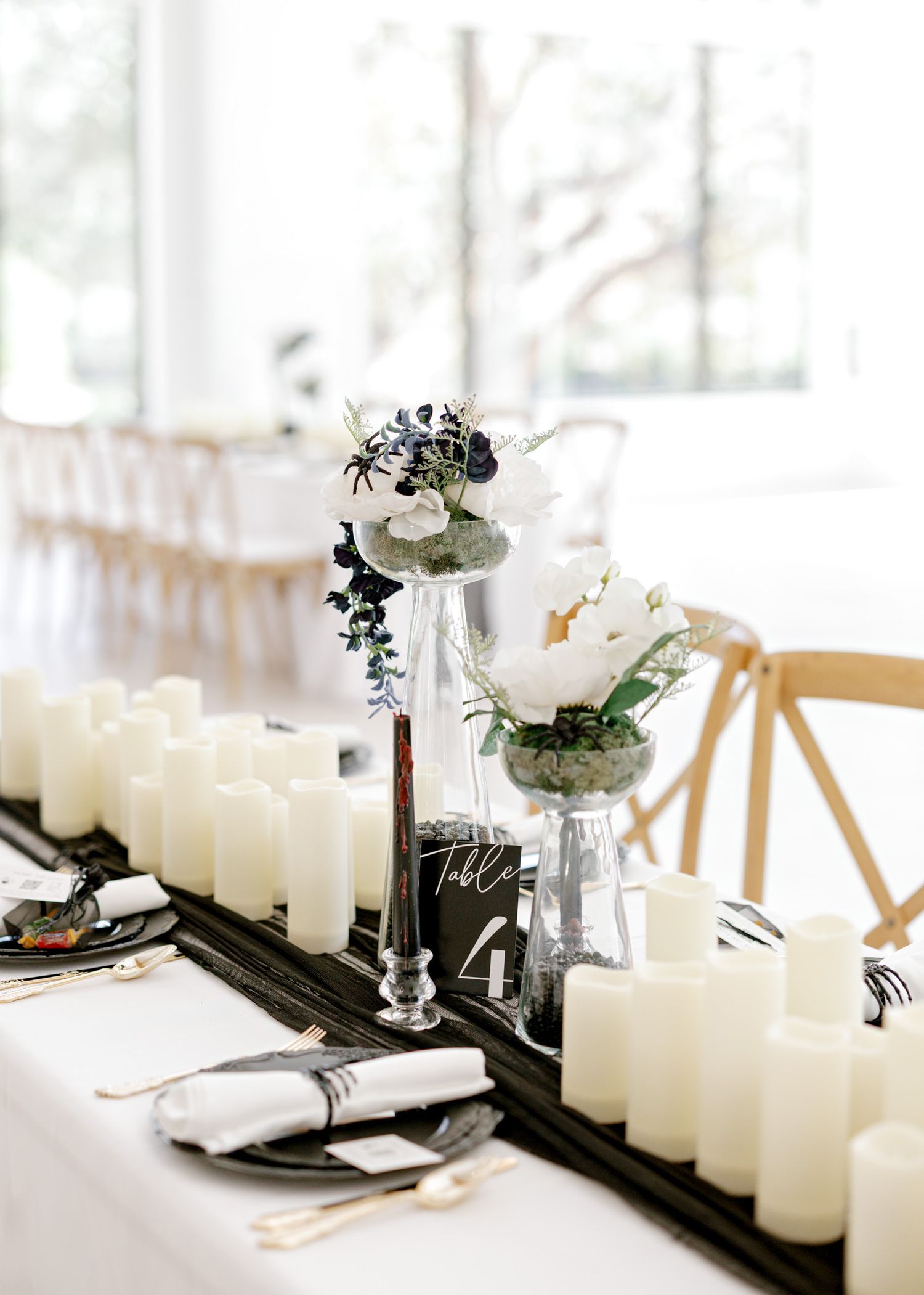 Elegant table setting with white pillar candles and greenery in a bright modern space.