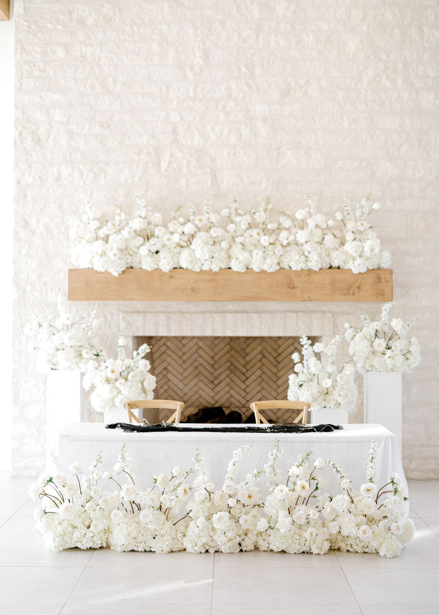 Modern white fireplace display with floating wooden shelf and delicate white floral arrangements.
