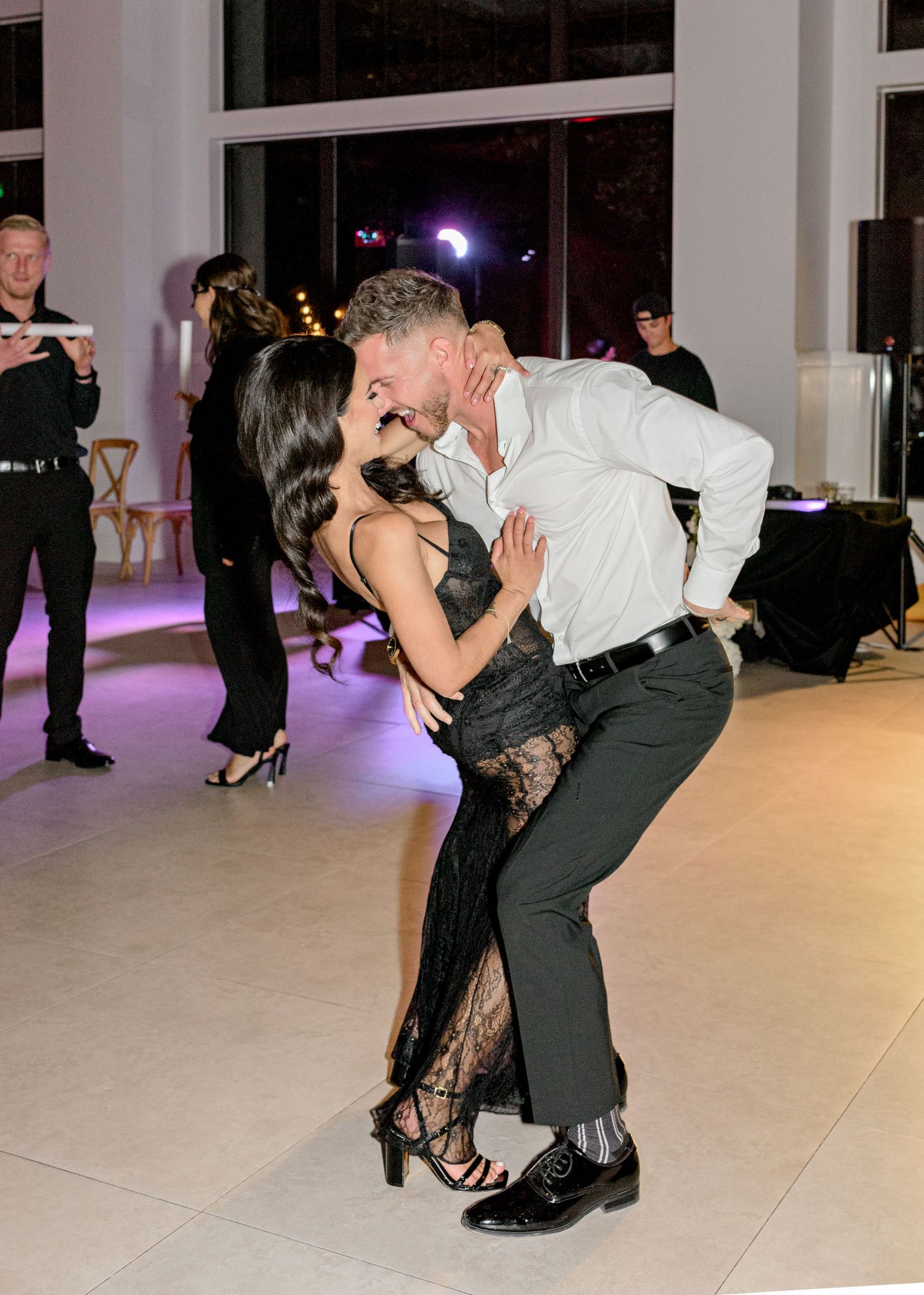 A couple performs an elegant dance dip during a wedding reception with purple ambient lighting in the background.